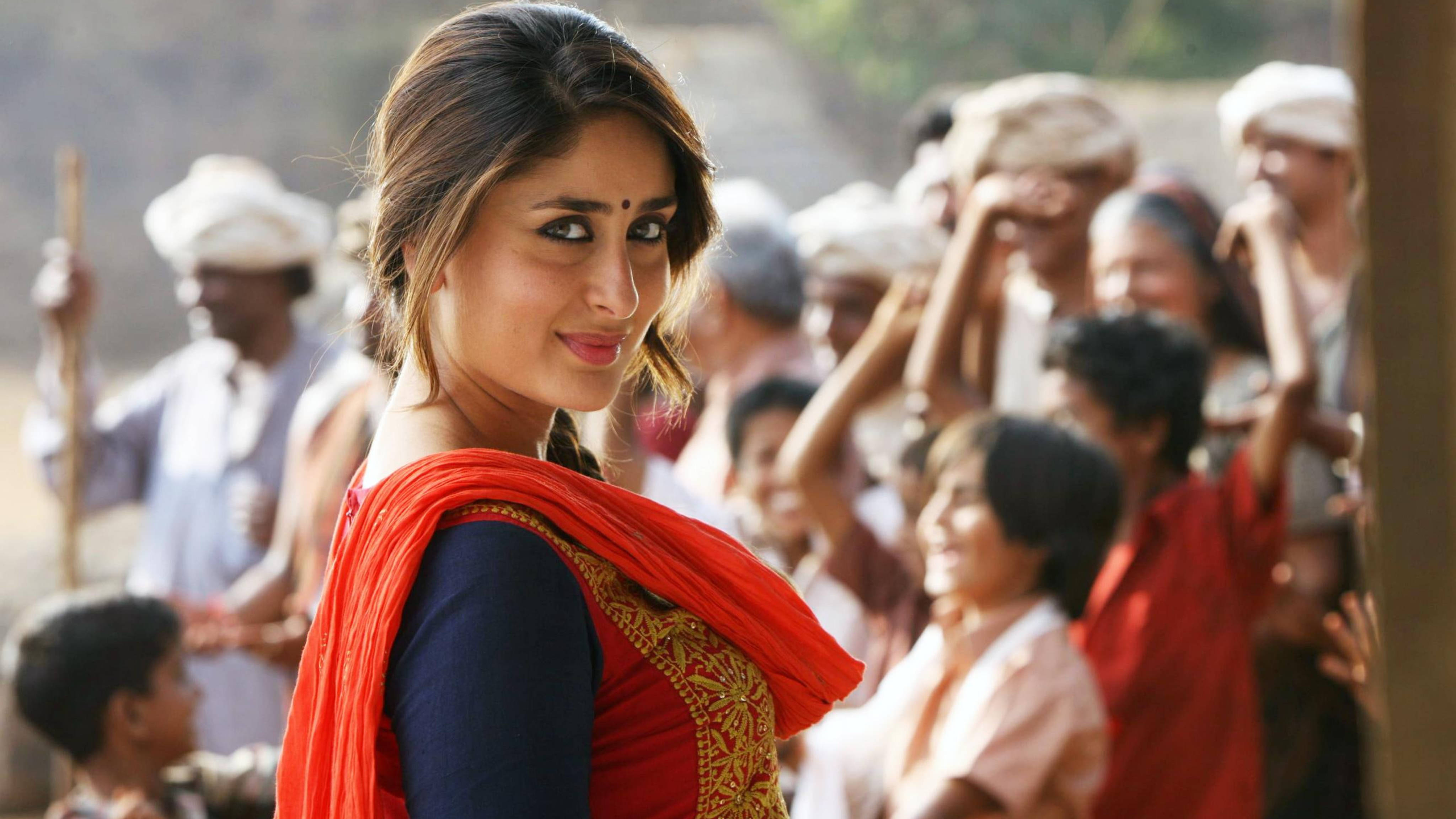 Kareena 桌布 壁紙 — 一位身穿鮮豔紅藍傳統服飾的女性自信地微笑，身後有群眾觀看。