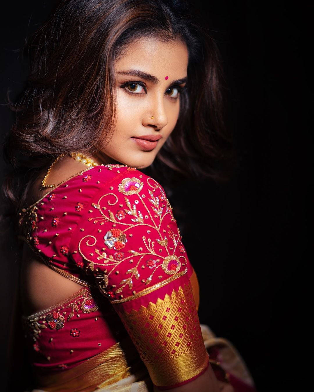 anupama parameswaran 桌布 壁紙 — 一位身穿鮮豔紅金刺繡傳統服飾的女性，在深色背景下轉身直視鏡頭。