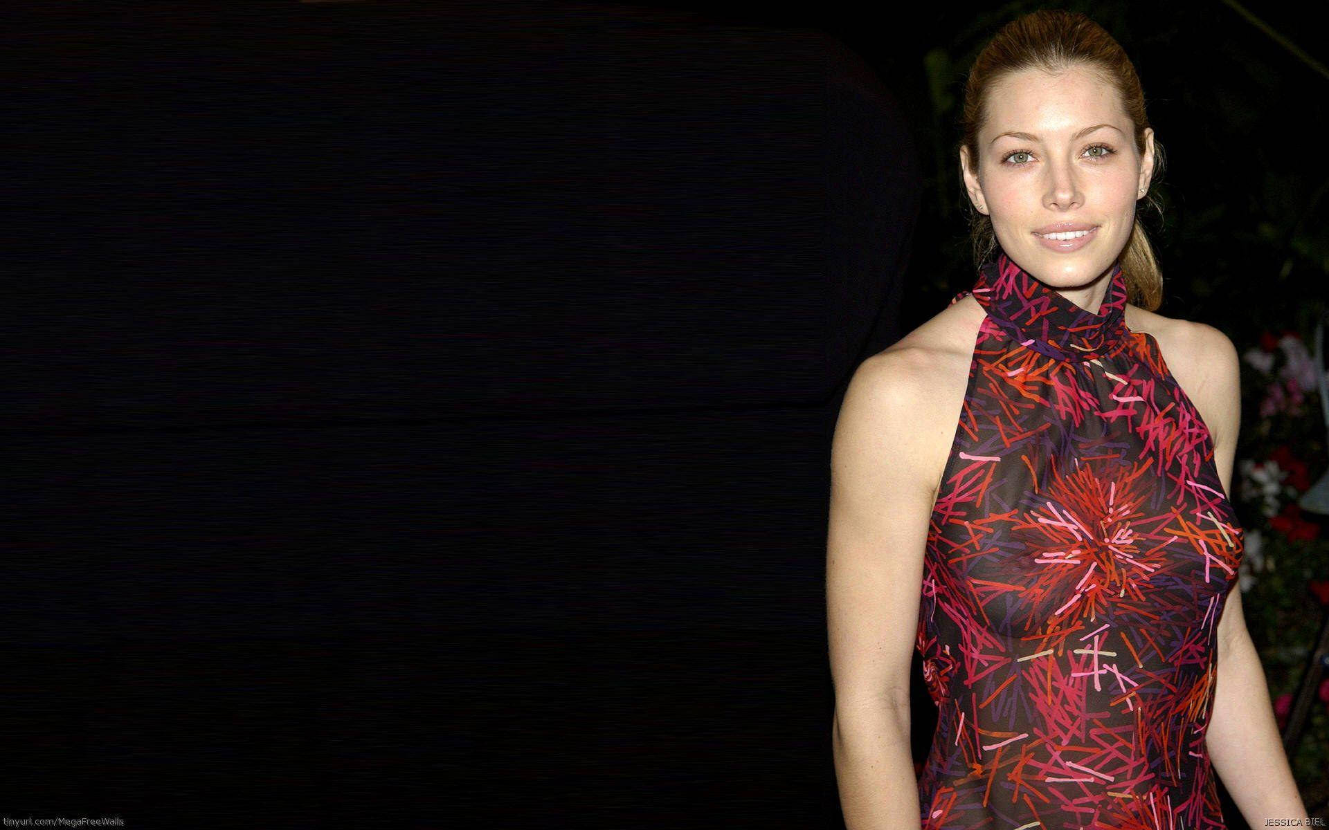 jessica biel 桌布 壁紙 — 一位身穿鮮豔紅黑圖案連衣裙的女性在深色背景下微笑。