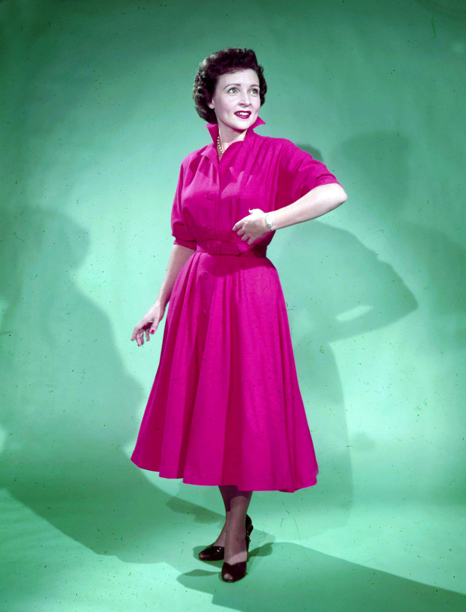 Betty White 桌布 壁紙 — 一位身穿鮮豔紫紅色連衣裙的女性在純綠色攝影棚背景前自信地擺姿勢，燈光效果戲劇化。