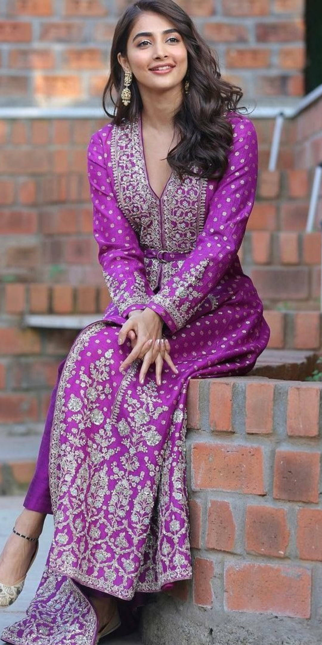 Indian 桌布 壁紙 — 一位身穿鮮豔紫色刺繡服裝的女性，坐在戶外的磚牆上微笑。