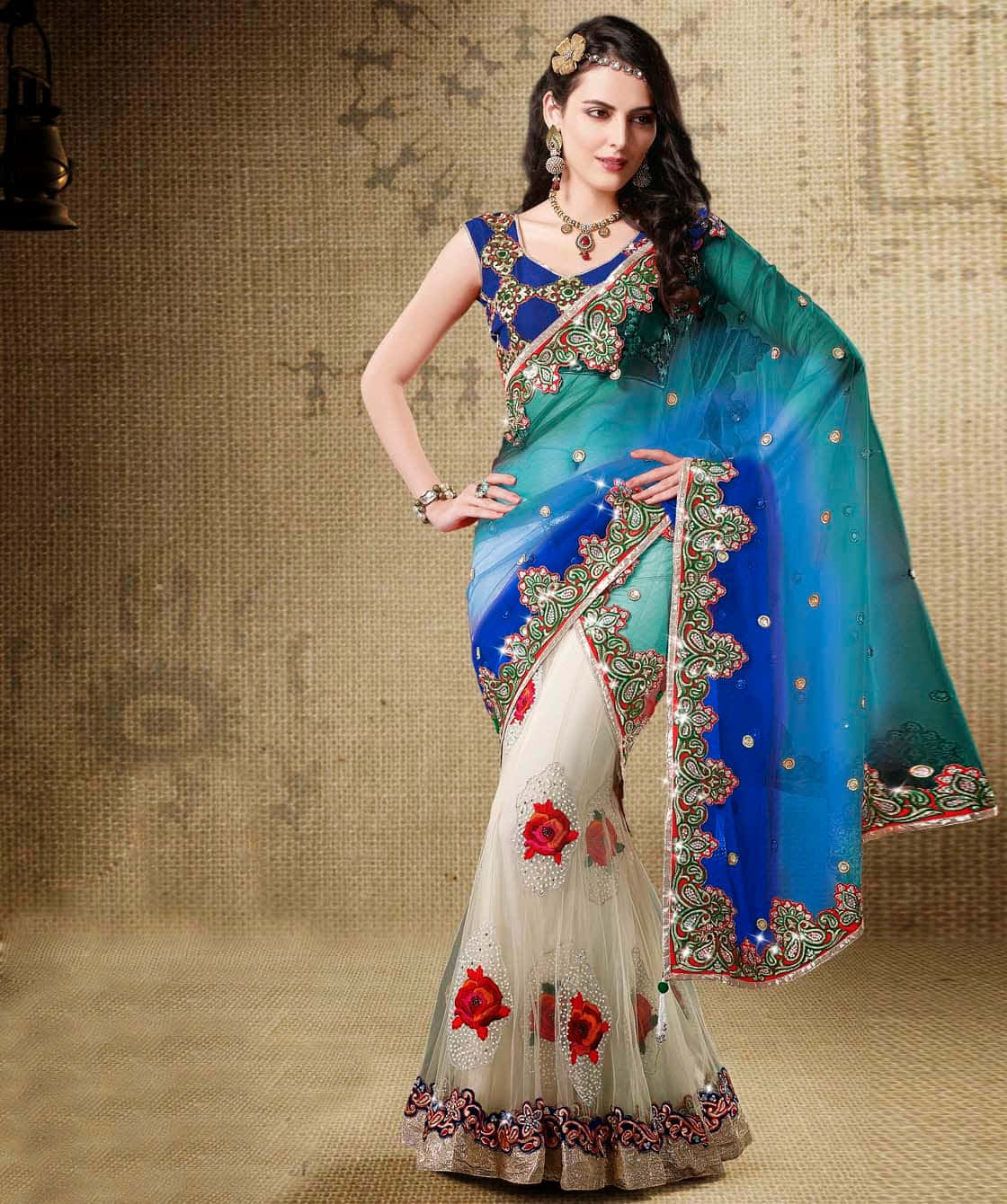Saree 桌布 壁紙 — 一位身穿鮮豔藍綠色刺繡紗麗、帶有紅色玫瑰圖案的女郎，在質感米色背景前自信地擺姿勢。