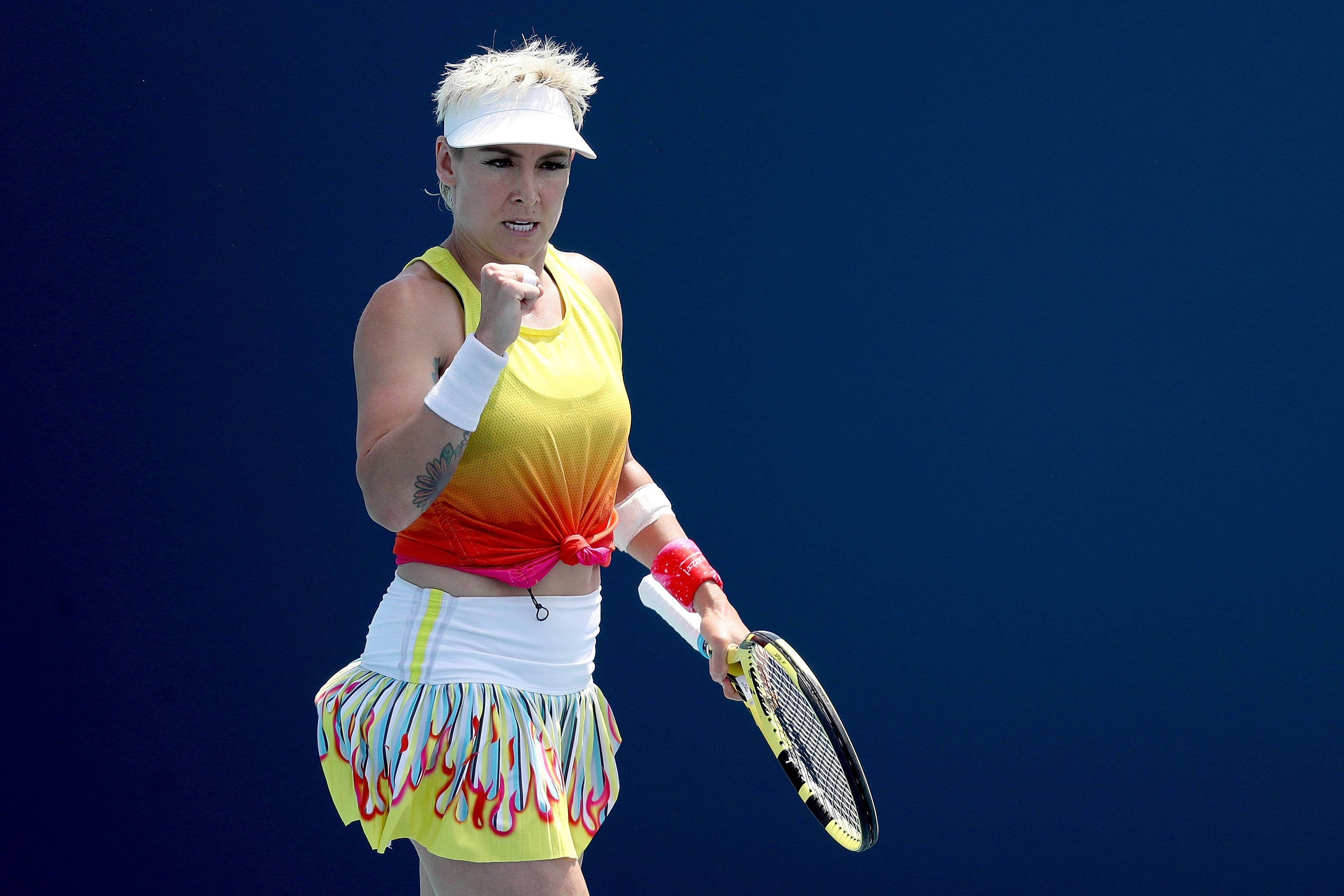 Tennis 桌布 壁紙 — 一位身穿鮮豔黃橙色服裝的女網球運動員，在純藍色背景前握緊拳頭慶祝。