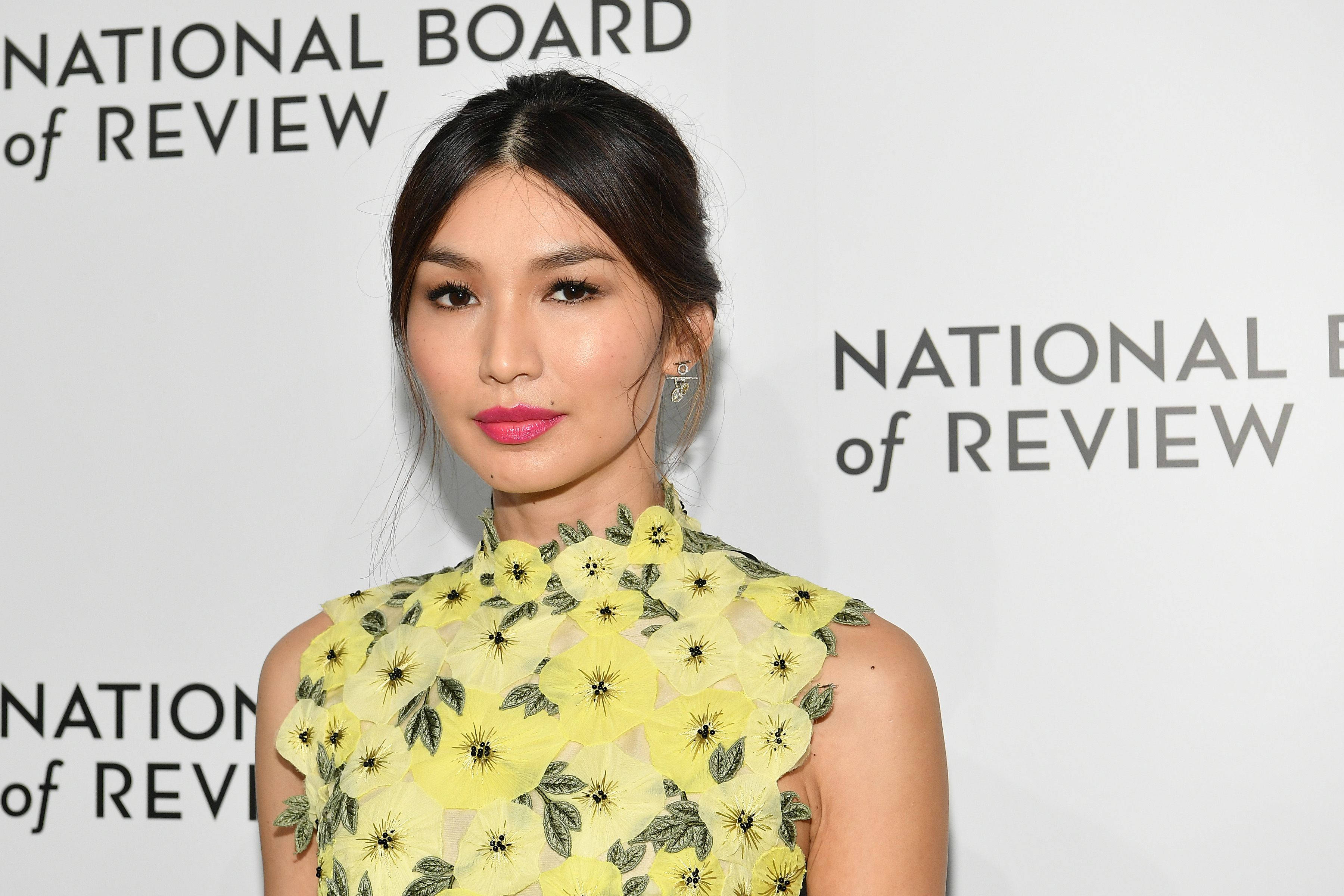 Gemma Chan 桌布 壁紙 — 一位身穿鮮豔黃色花卉連衣裙的女性在國家評論委員會活動中自信地擺姿勢，背景是潔白的。