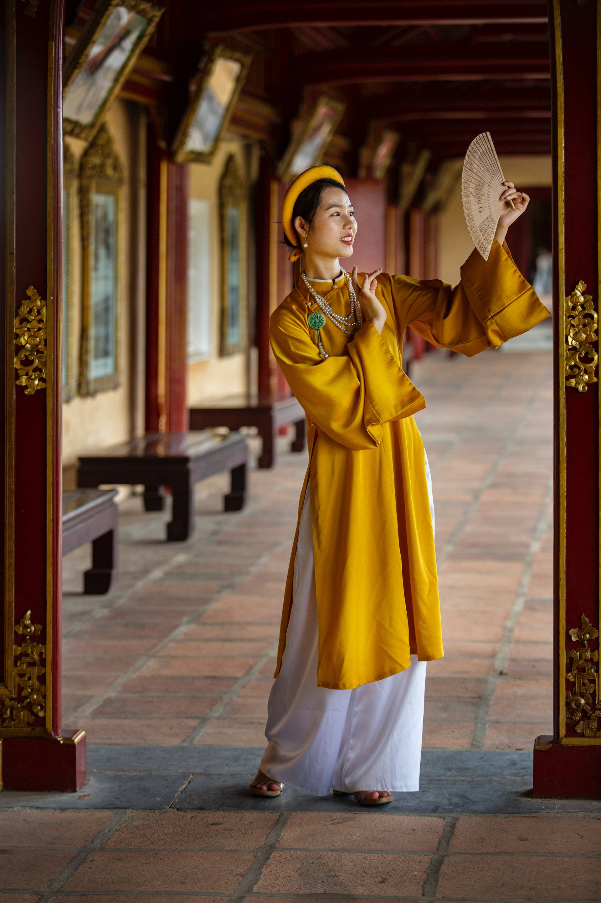 Woman 桌布 壁紙 — 一位身穿鮮黃色傳統服飾的女性，優雅地拿著扇子，站在紅色木造寺廟走廊中。