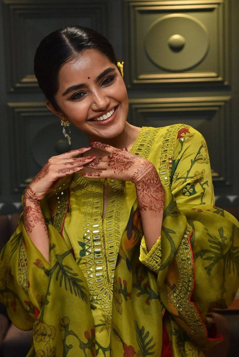 anupama parameswaran 桌布 壁紙 — 一位身穿鮮黃色刺繡服裝、容光煥發的女性，手上帶有複雜的指甲花圖案，溫暖地微笑。