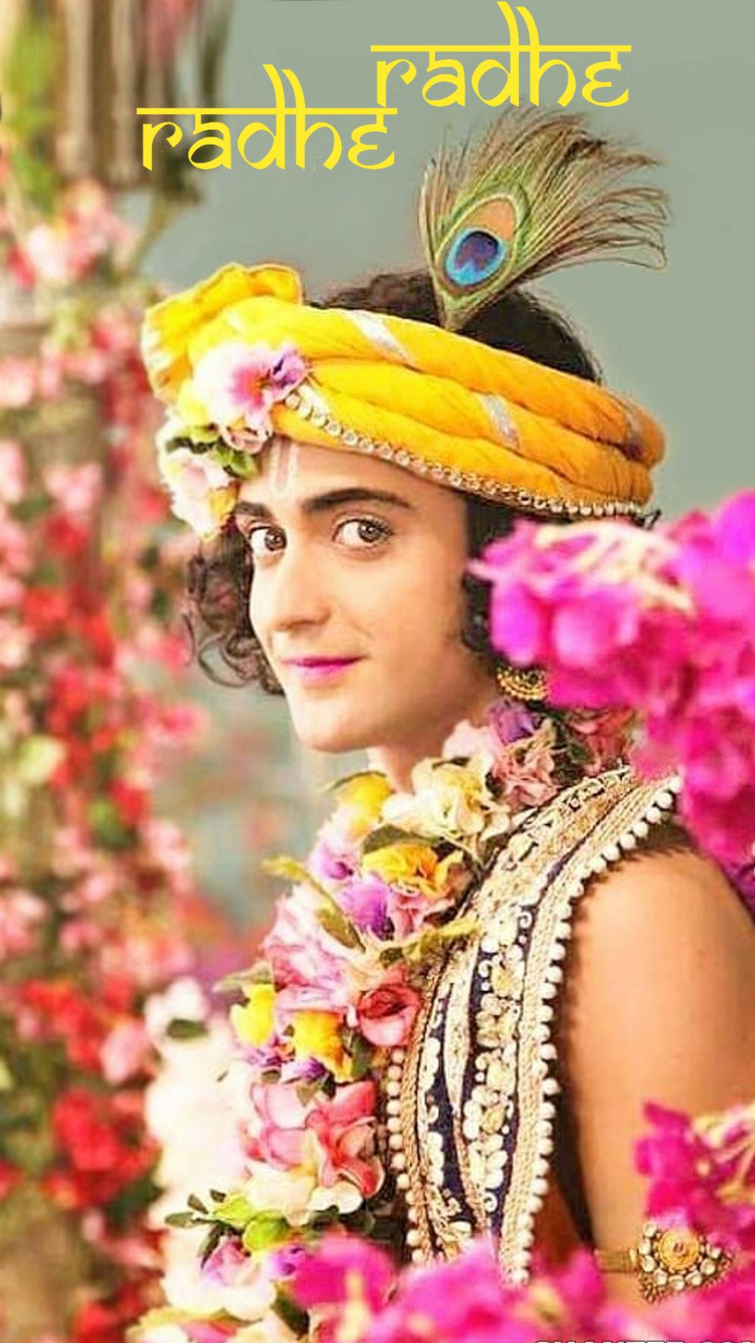 radha krishna serial 桌布 壁紙 — 一位身穿鮮黃色服飾和花環的人，在粉紅色和紅色花朵的瀑布中微笑。
