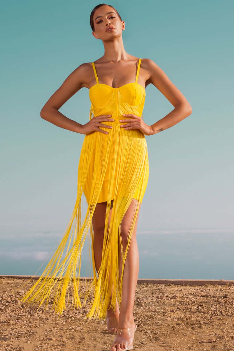 Yellow Fashion 桌布 壁紙 — 一位身穿鮮黃色流蘇裙的女性，在晴朗的藍天下自信地站在沙漠景觀中。