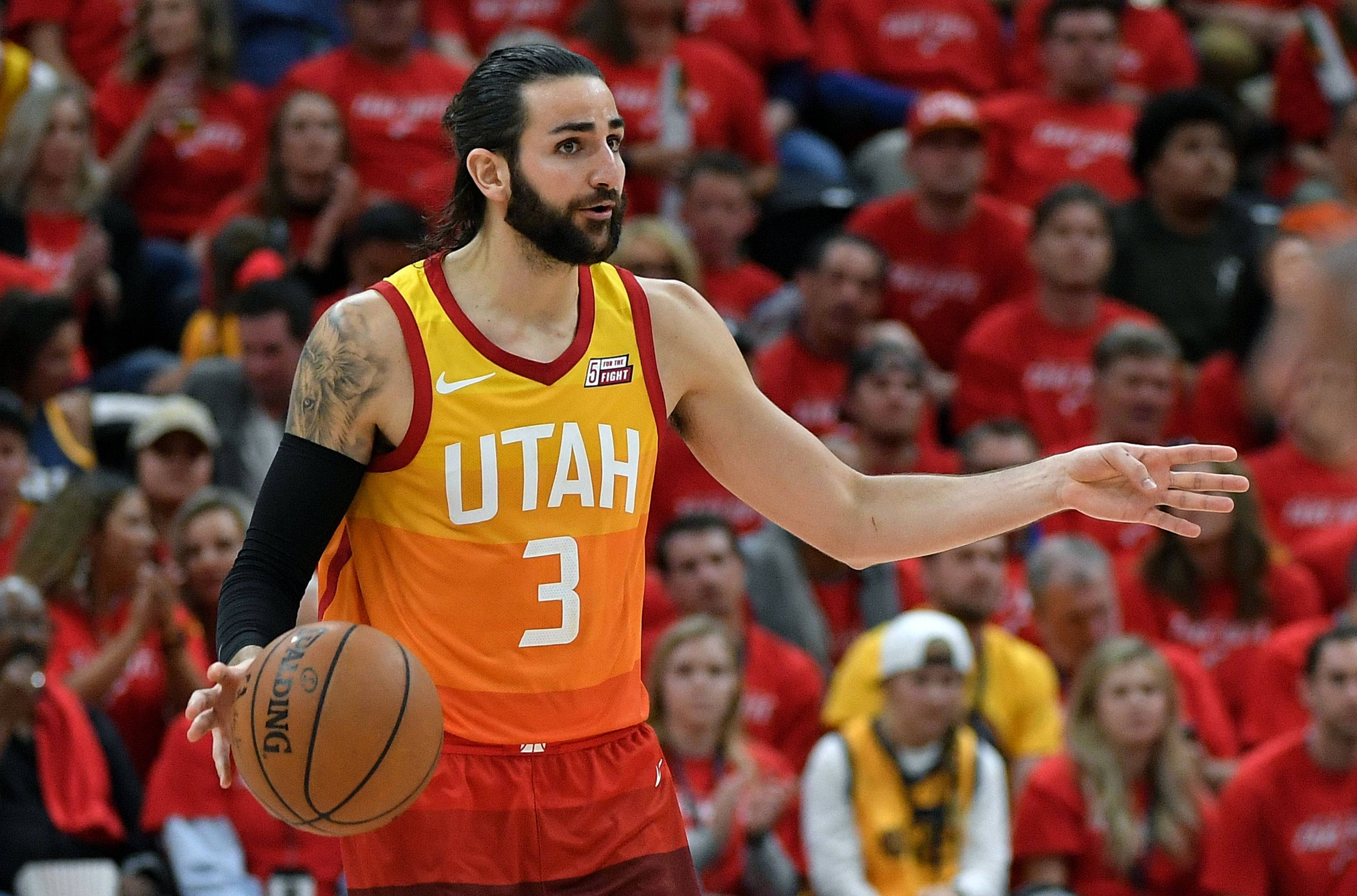 Ricky Rubio 桌布 壁紙 — 一位身穿黃橙色球衣的猶他爵士籃球運動員在比賽中持球並做手勢，背景有身穿紅色衣服的球迷。