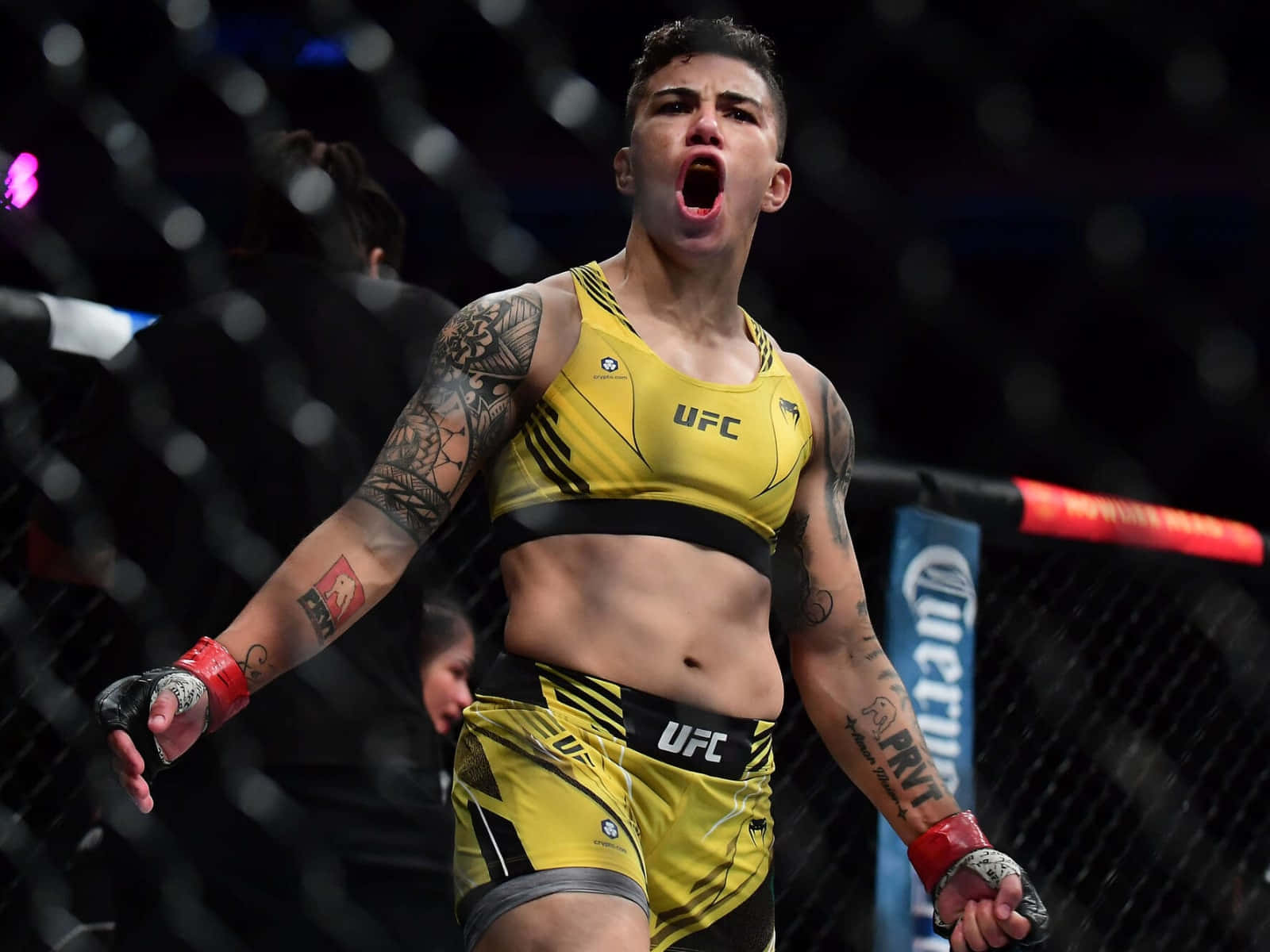 MMA 桌布 壁紙 — 一位身穿黃色UFC裝備的女性MMA拳手在昏暗的八角籠內發出勝利的咆哮。