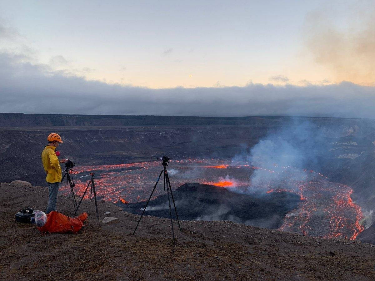 Volcano 桌布 壁紙 — 一位身穿黃色外套的攝影師在黃昏時捕捉到流經火山口的發光熔岩。