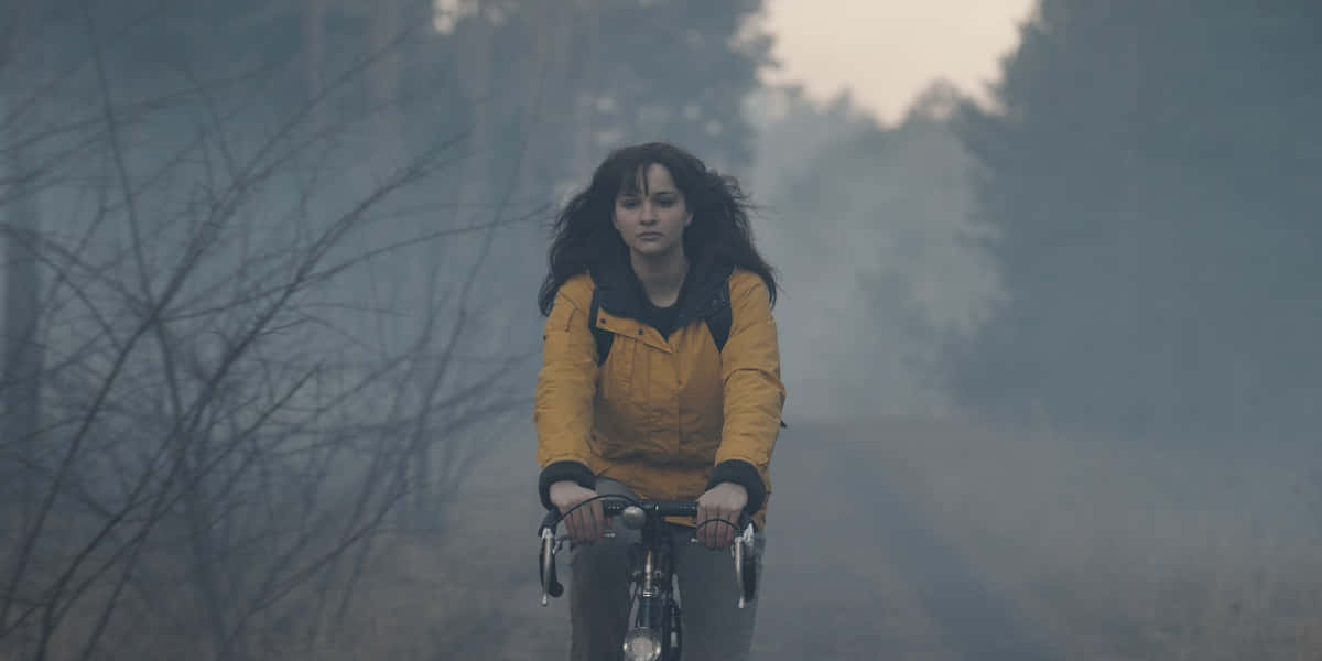 Raincoat 桌布 壁紙 — 一位身穿黃色夾克的女士騎著自行車穿過霧氣瀰漫的森林，樹木光禿，光線柔和擴散。