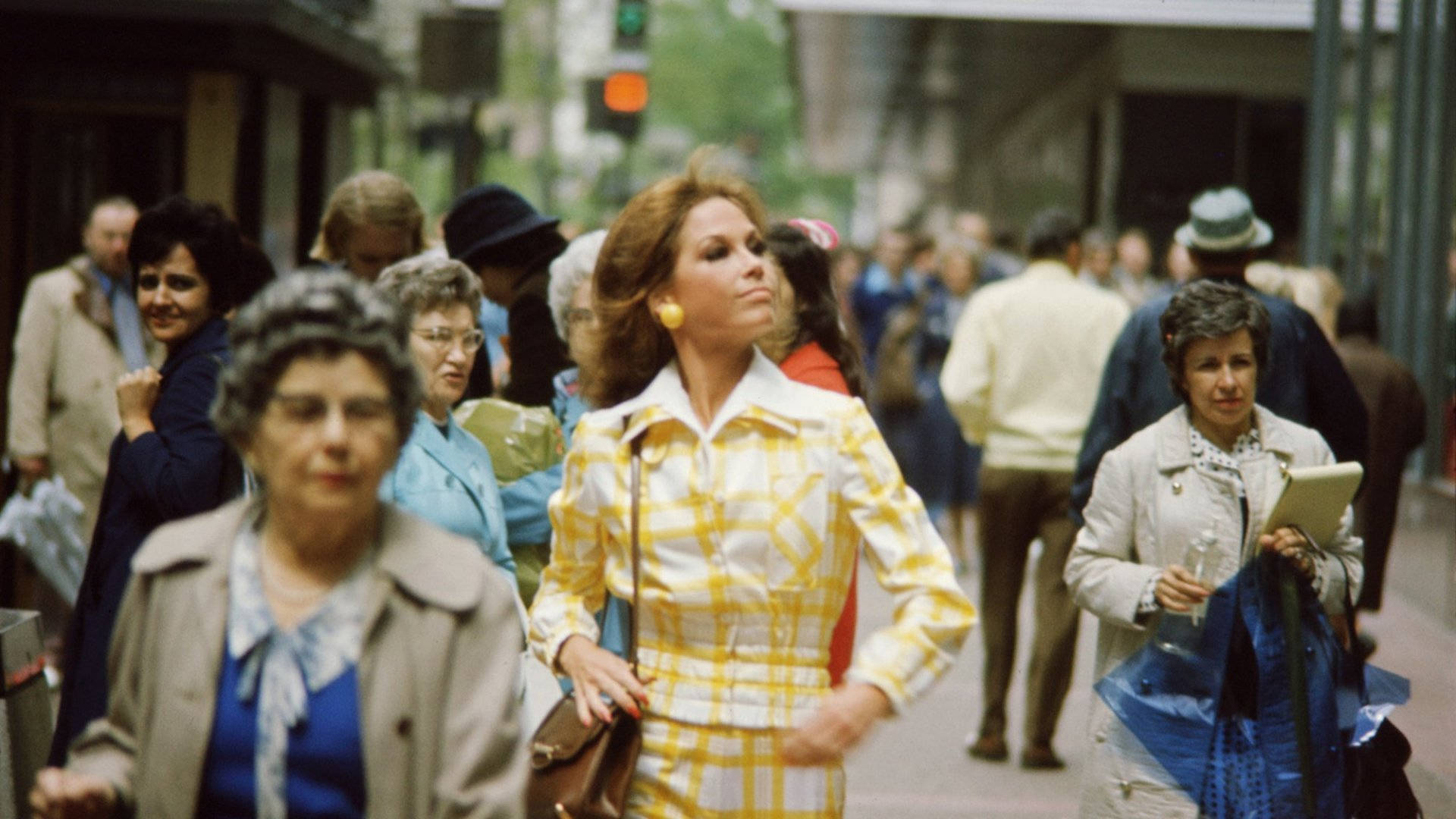 復古 桌布 壁紙 — 一位身穿黃色格子西裝的女性自信地穿過1970年代繁忙的城市街道，周圍都是行人。