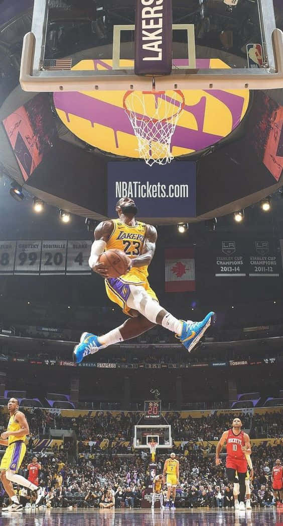 King LeBron James 桌布 壁紙 — 一位身穿黃色湖人球衣的籃球運動員在紫色和金色的籃框下空中灌籃，下方是座無虛席的球場。