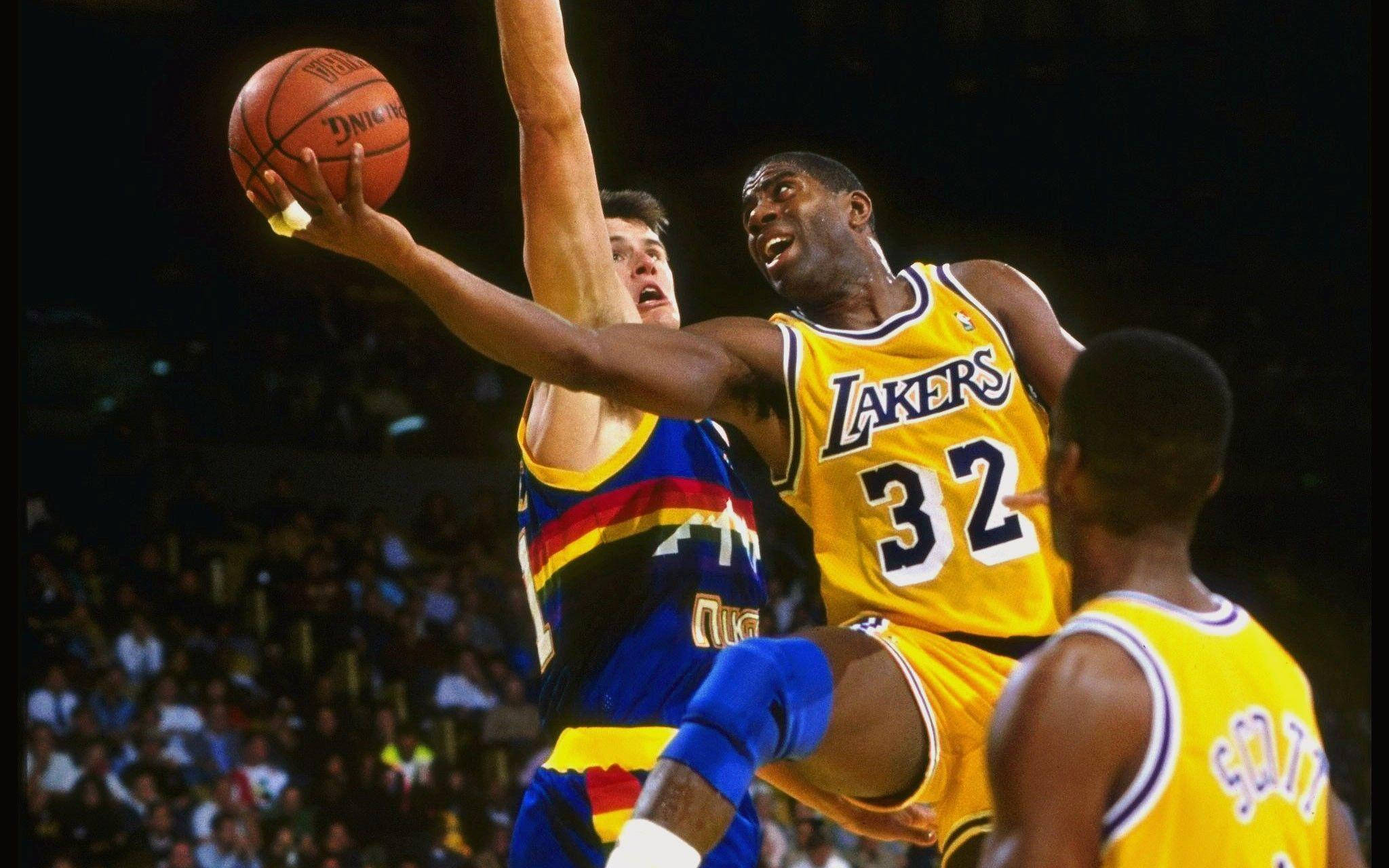 Magic Johnson 桌布 壁紙 — 一位身穿黃色球衣32號的湖人球員跳起投籃，同時被一位身穿藍紅球衣的對手在場館燈光下防守。