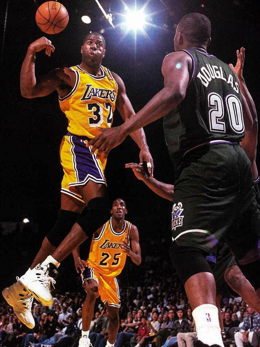 Magic Johnson 桌布 壁紙 — 一位身穿黃色球衣的湖人球員跳起投籃，而一位身穿黑色球衣的國王防守球員在場館燈光下干擾投籃。