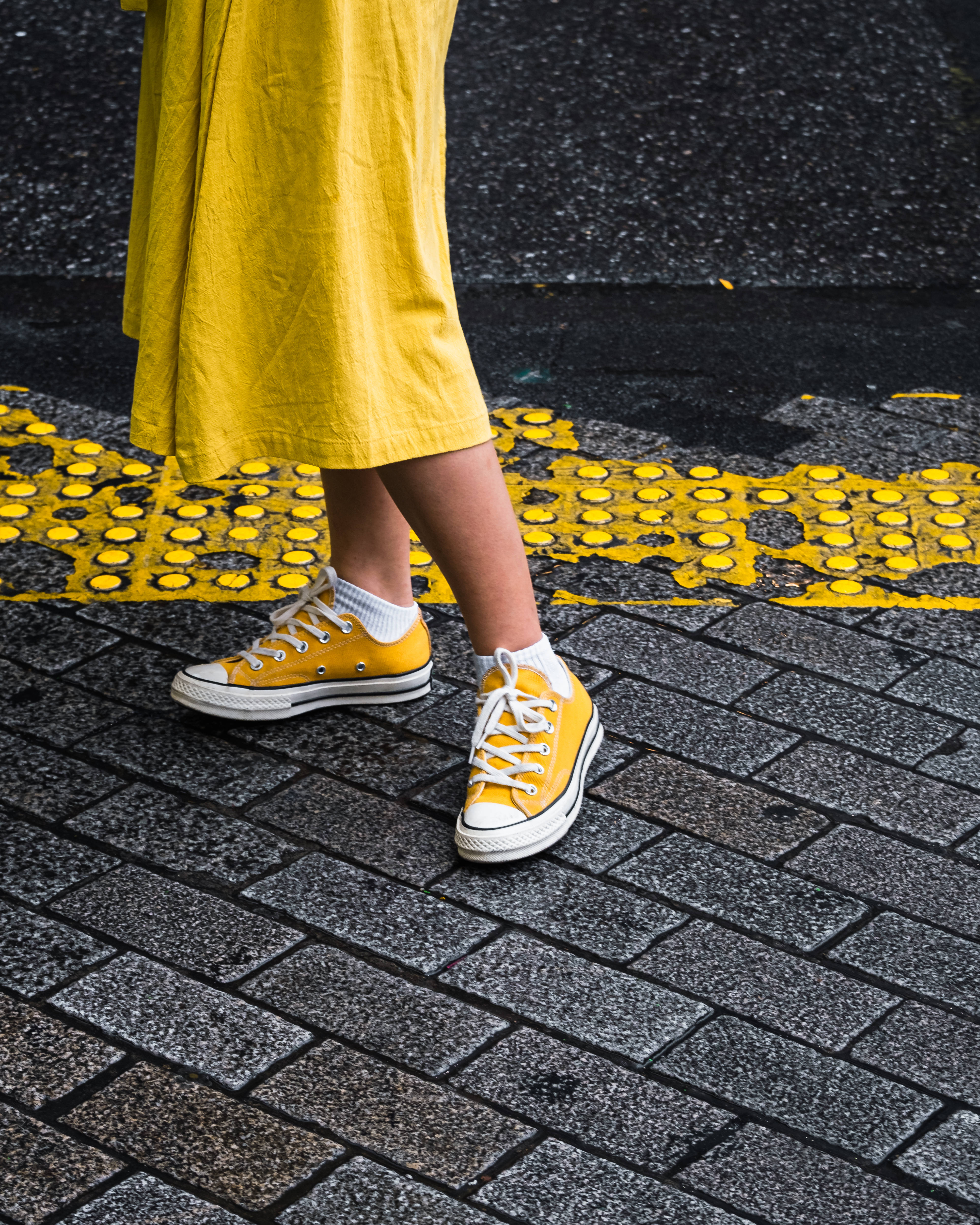 Converse 桌布 壁紙 — 一位身穿黃色連衣裙和黃色運動鞋的人，在灰色磚砌人行道上沿著黃色觸覺引道帶行走。