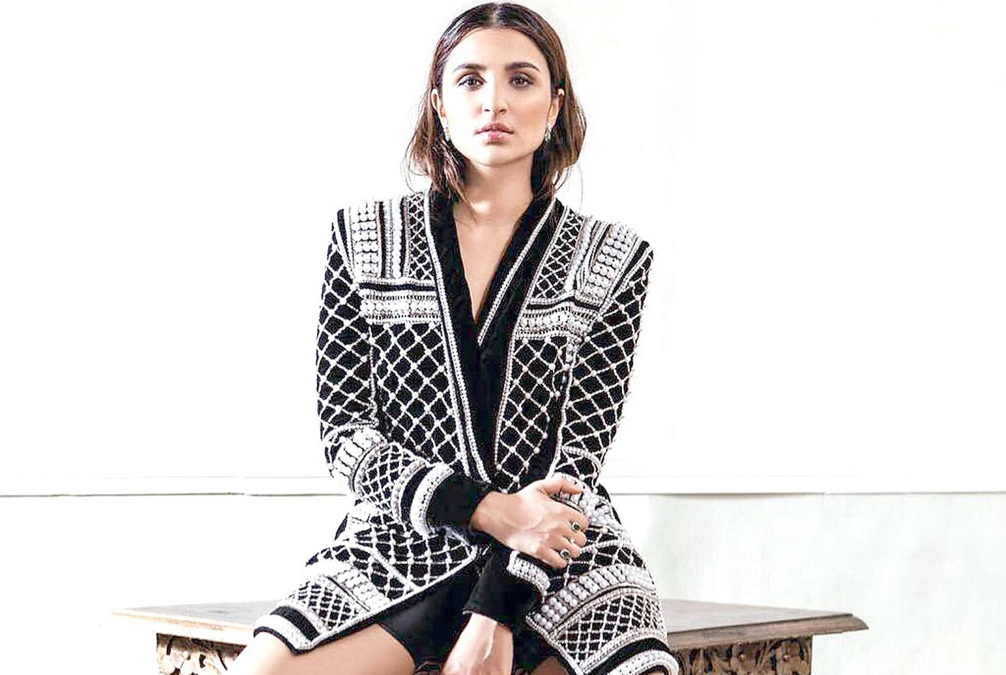 Parineeti 桌布 壁紙 — 一位身穿黑白圖案外套的女性，端坐在白色牆壁前的木長椅上。