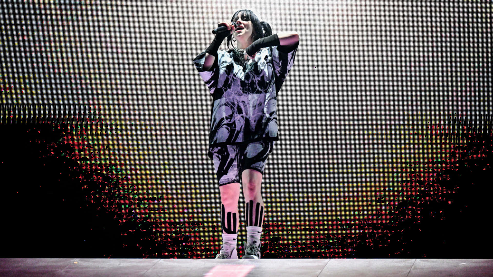 Billie Eilish Laptop 桌布 壁紙 — 一位身穿黑白圖案服裝的表演者在舞台上熱情演唱，背景是像素化的LED螢幕。