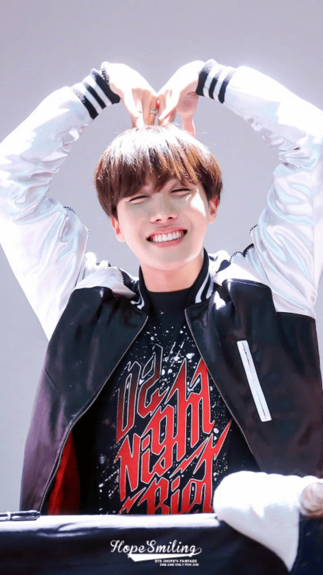 jhope 桌布 壁紙 — 一位身穿黑白外套的年輕男子微笑著，雙手在頭頂比出心形。