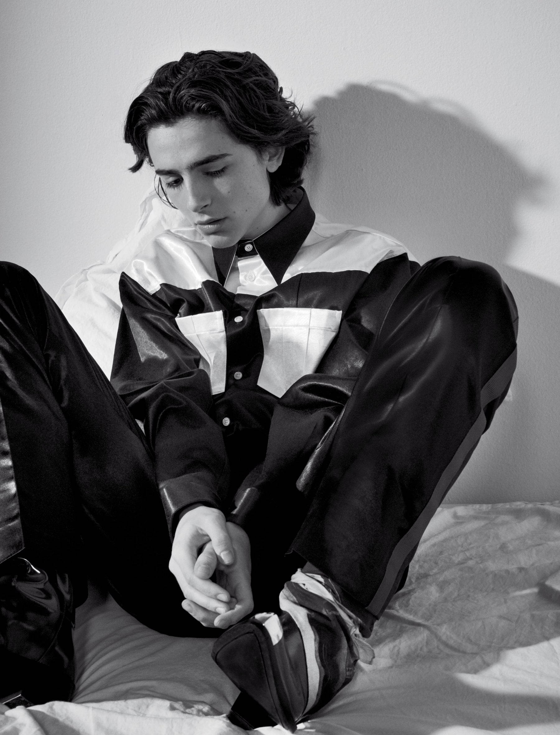 Timothée Chalamet 桌布 壁紙 — 一位身穿黑白皮革套裝的年輕男子，在戲劇性的光影效果下沉思地坐在床上。