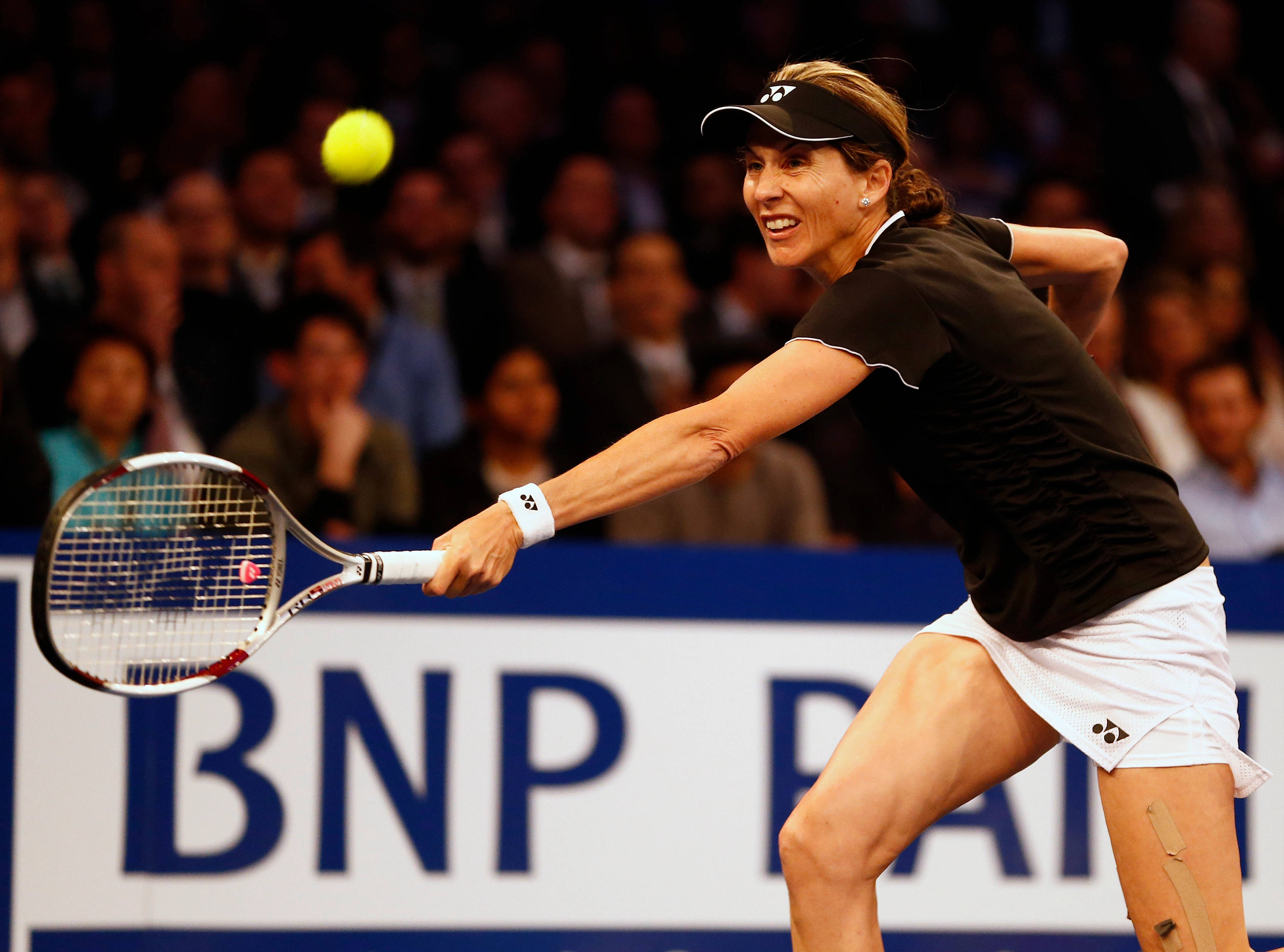 Monica Seles 桌布 壁紙 — 一位身穿黑白裝備的女網球選手在體育館燈光下進行激烈比賽時，揮拍擊向一顆亮黃色的球。