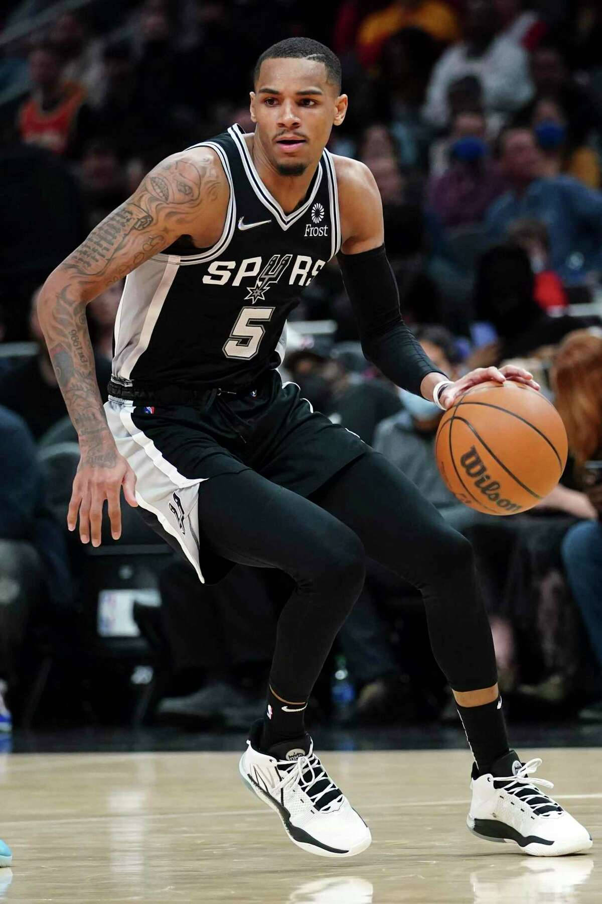 Dejounte Murray 桌布 壁紙 — 一位身穿黑白馬刺球衣的籃球運動員在明亮的場館燈光下，專注地運球進行比賽。
