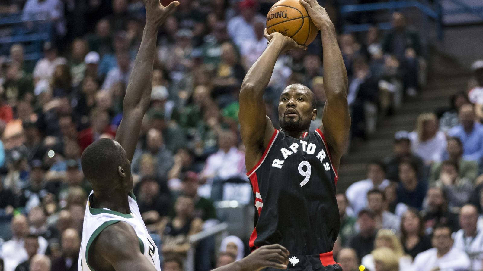 serge ibaka 桌布 壁紙 — 一位身穿黑色9號球衣的多倫多暴龍隊球員正在投籃，而一位身穿白色的防守球員在擠滿觀眾的場館中試圖封阻他。