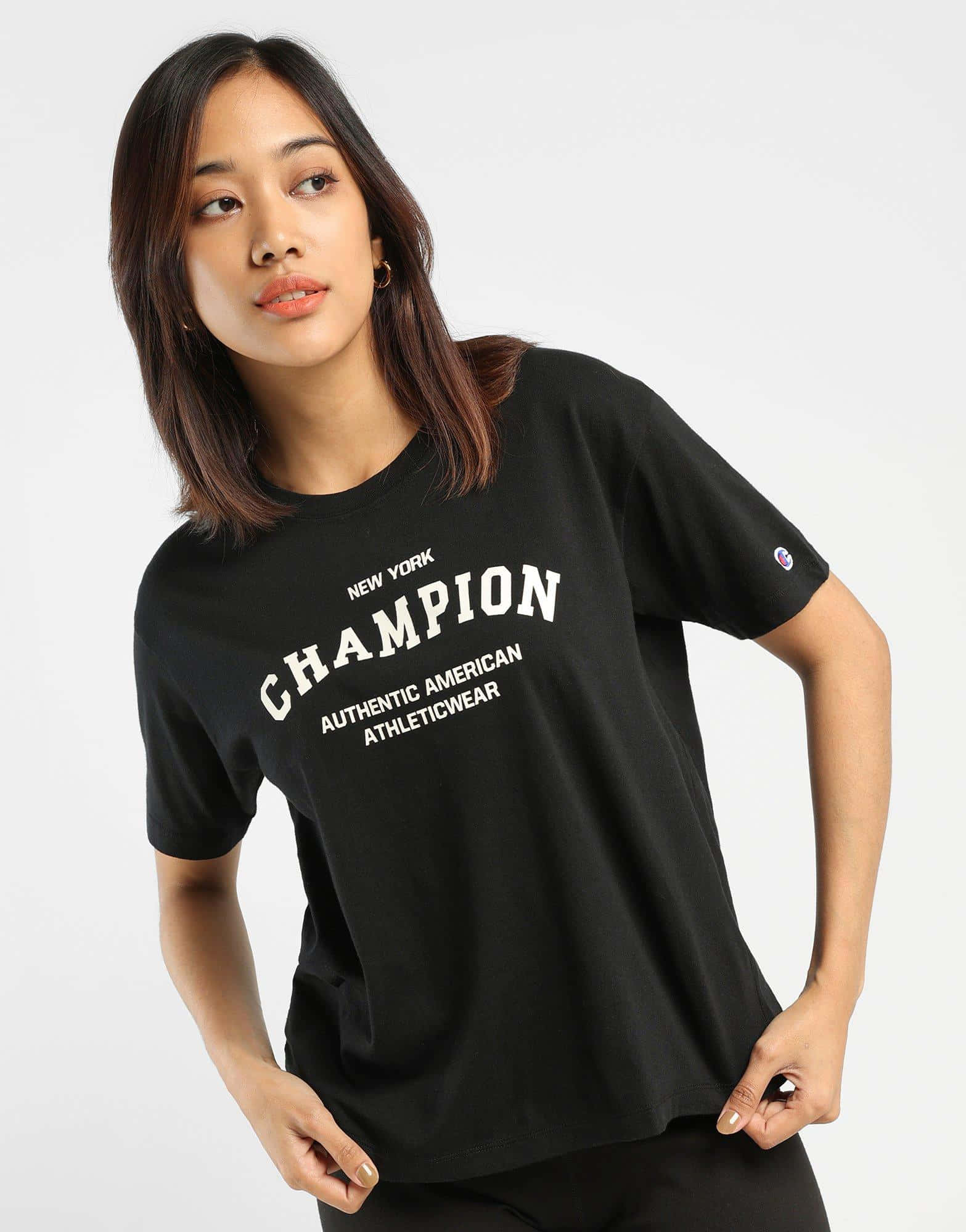 Champion 桌布 壁紙 — 一位身穿黑色Champion T恤的女性在柔和的攝影棚燈光下，自信地站在純白背景前擺姿勢。