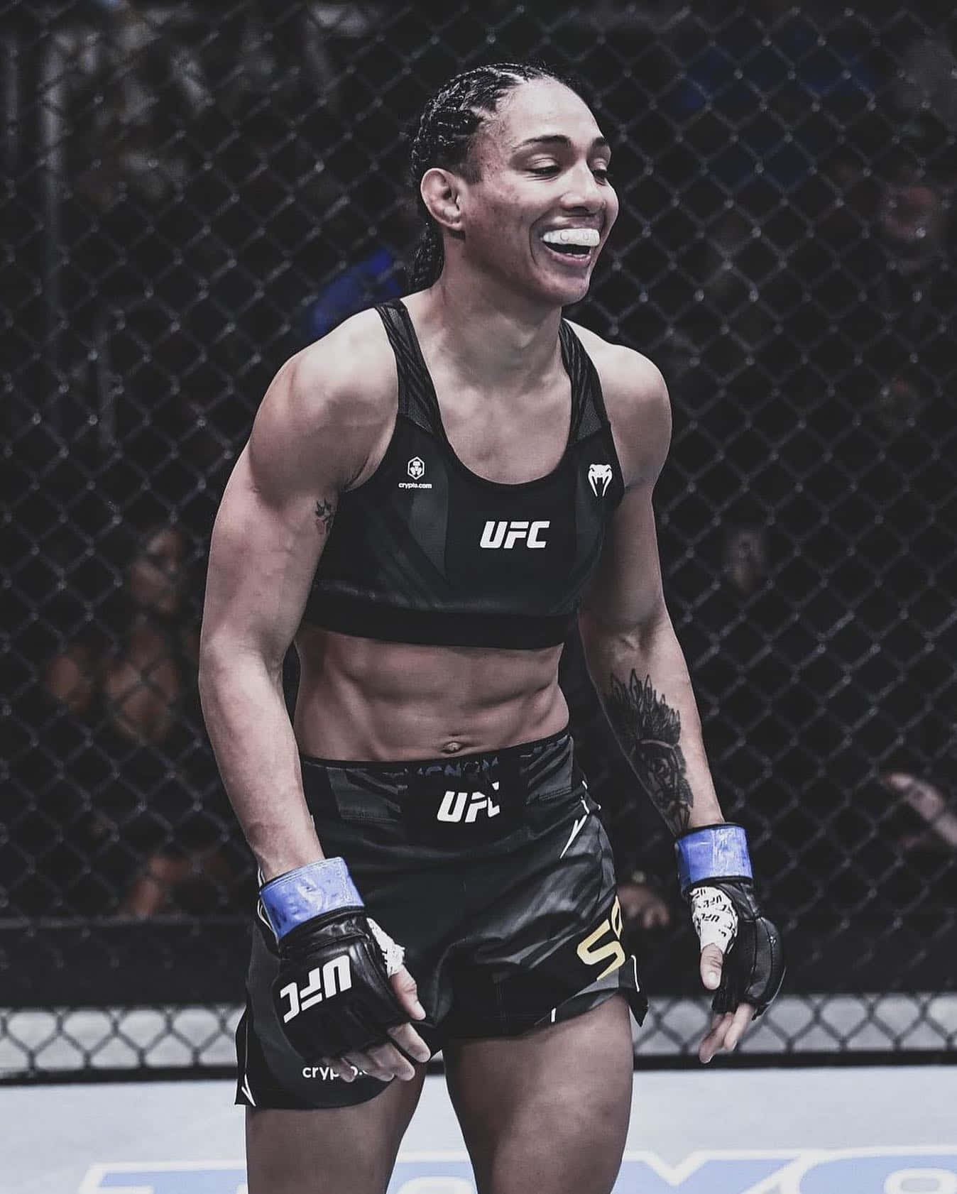 UFC 桌布 壁紙 — 一位身穿黑色UFC裝備的勝利女性MMA拳手在八角籠內開懷大笑。