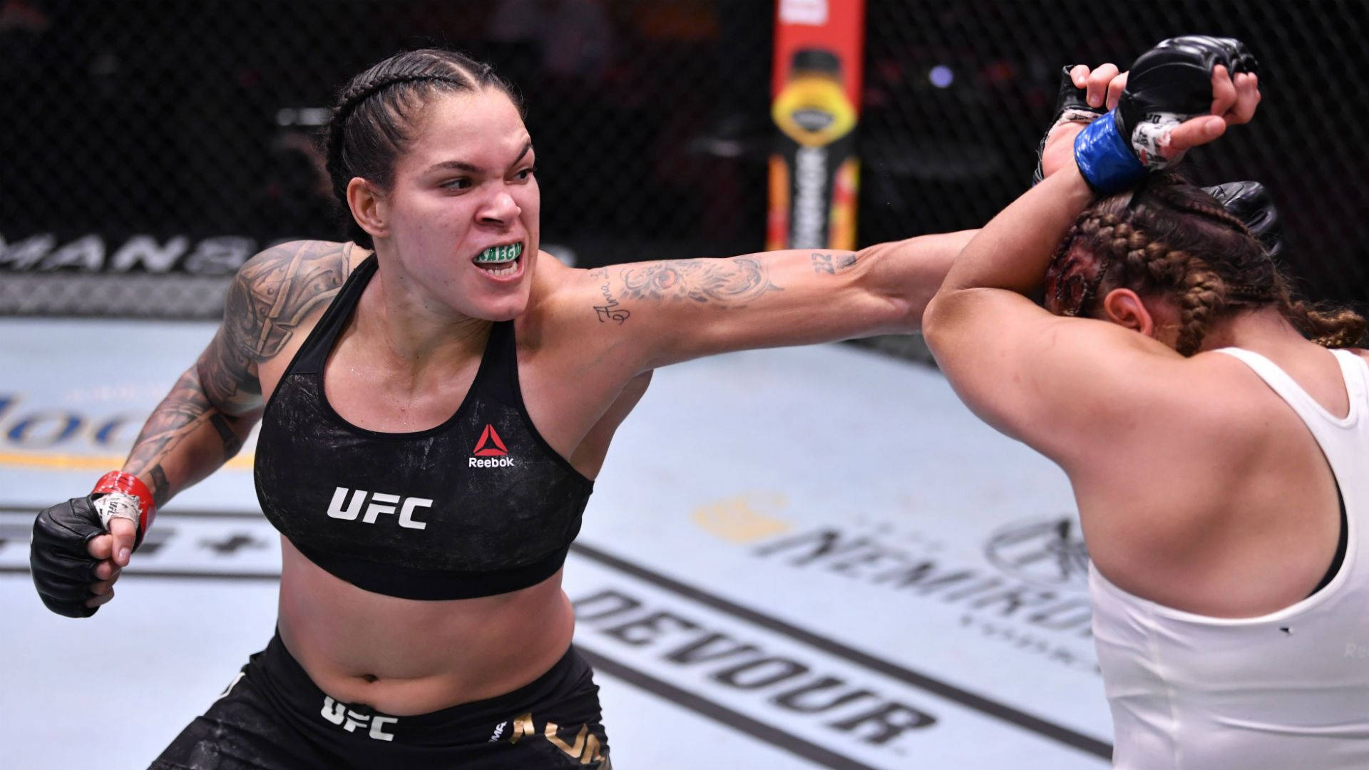 MMA 桌布 壁紙 — 一位身穿黑色UFC裝備的女性MMA拳手在八角籠內向對手打出強力一拳。
