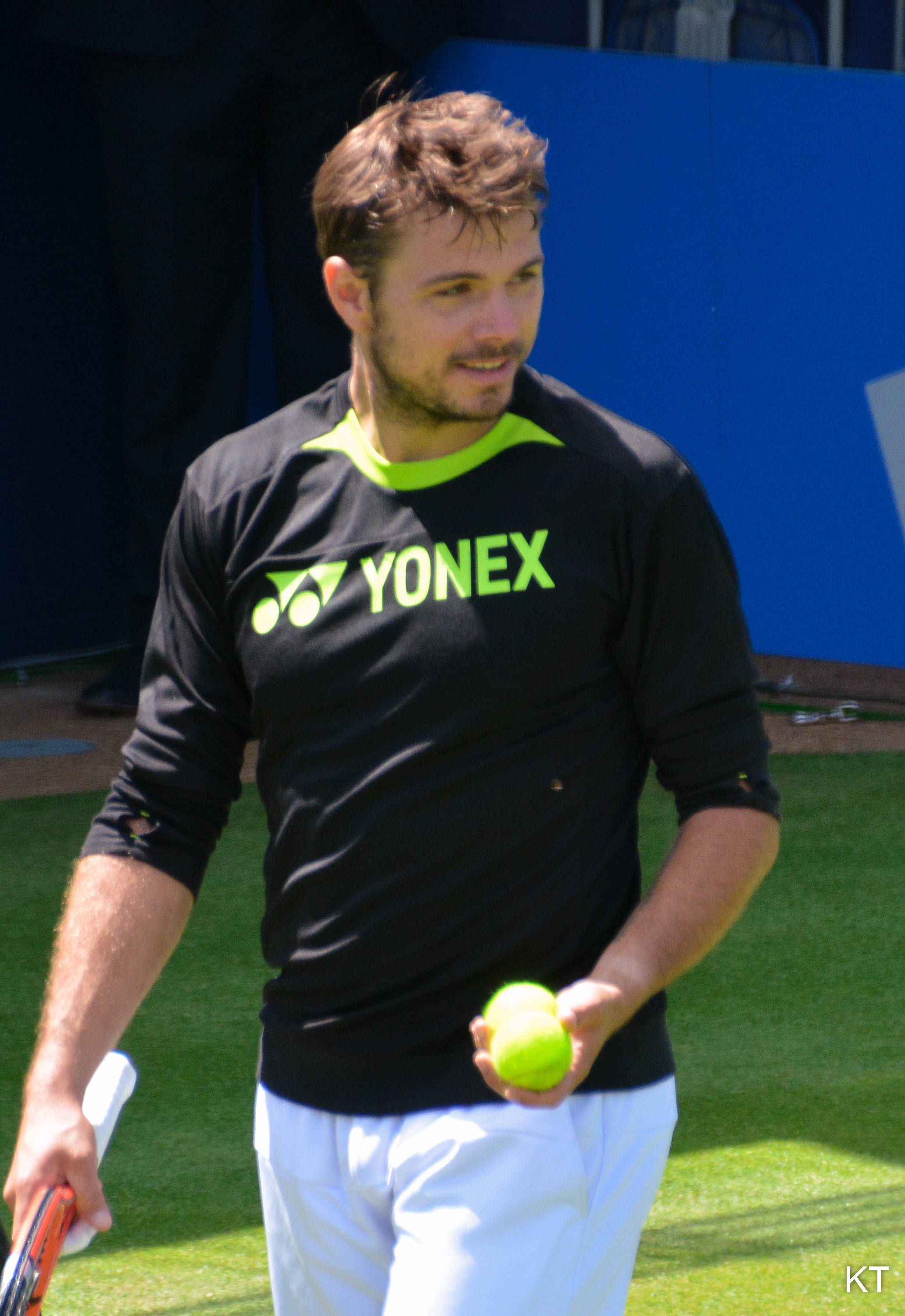 Tennis 桌布 壁紙 — 一位身穿黑色Yonex球衣的男性網球選手，在陽光明媚的草地場上拿著亮綠色的球和球拍。