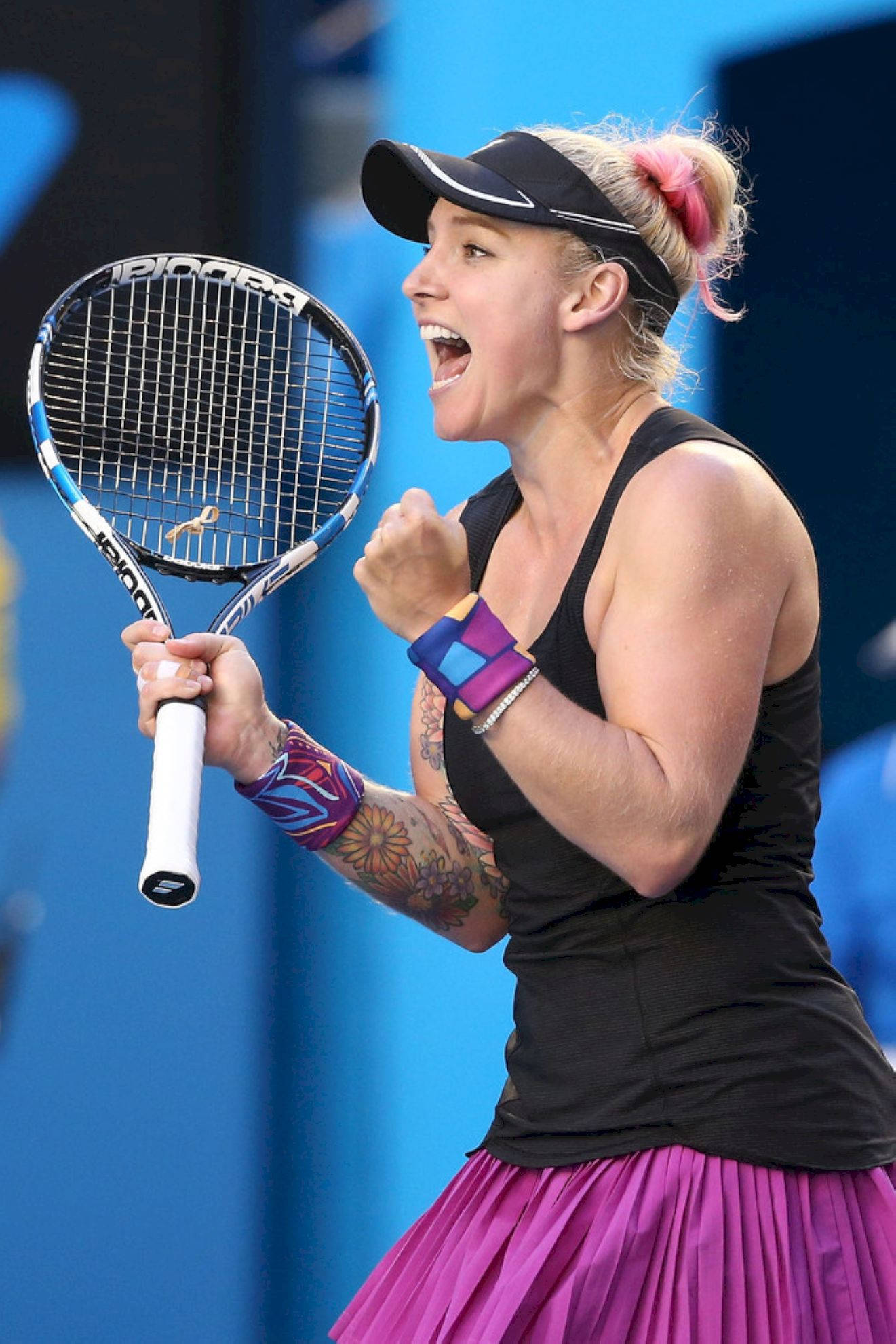 Tennis 桌布 壁紙 — 一位身穿黑色上衣和粉紅色裙子的女網球運動員在藍色球場背景下握緊拳頭並舉起球拍慶祝勝利。