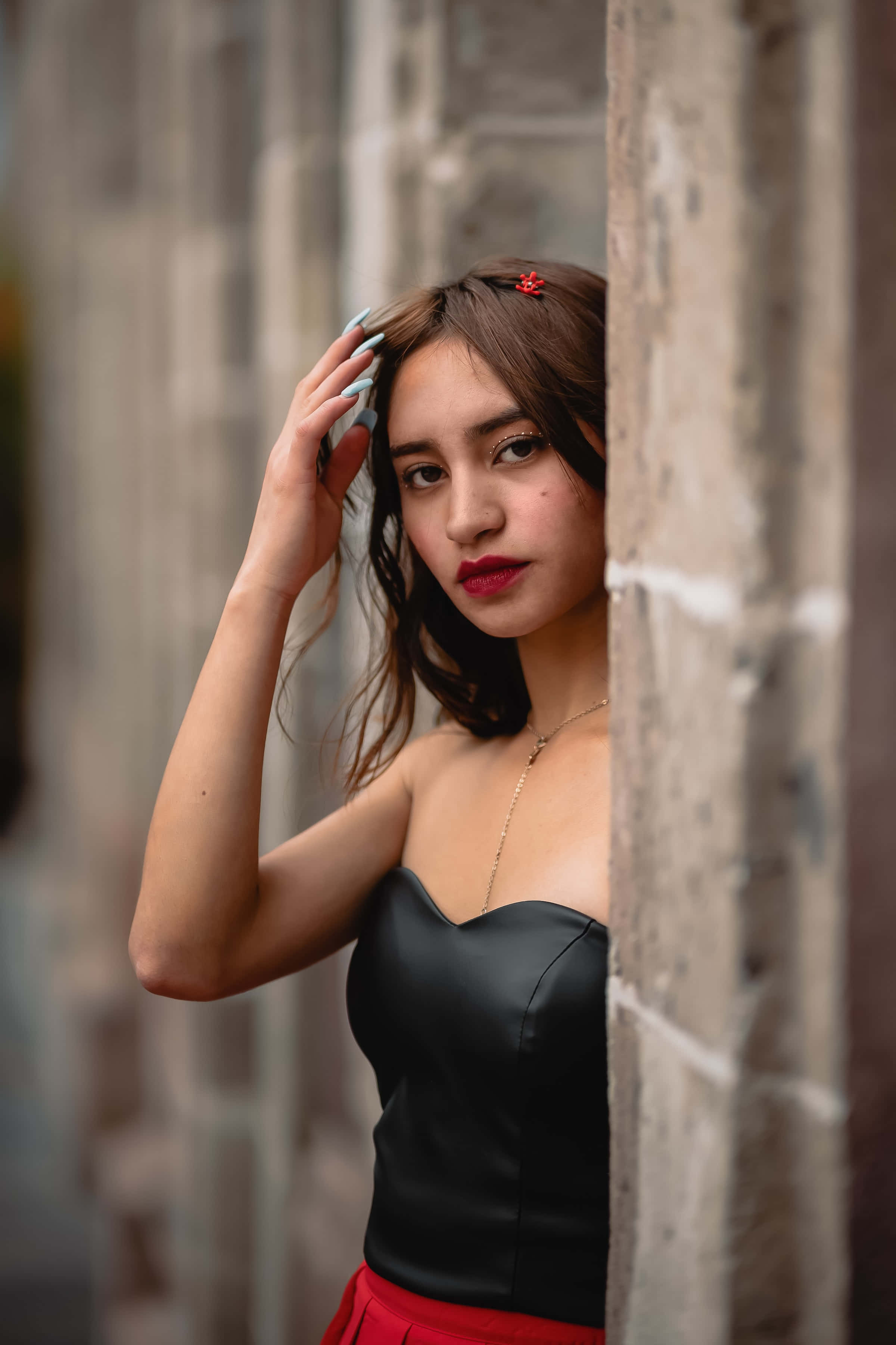 gorgeous 桌布 壁紙 — 一位身穿黑色上衣和紅色裙子的年輕女子從石牆後探出頭來，一手撥弄著頭髮。
