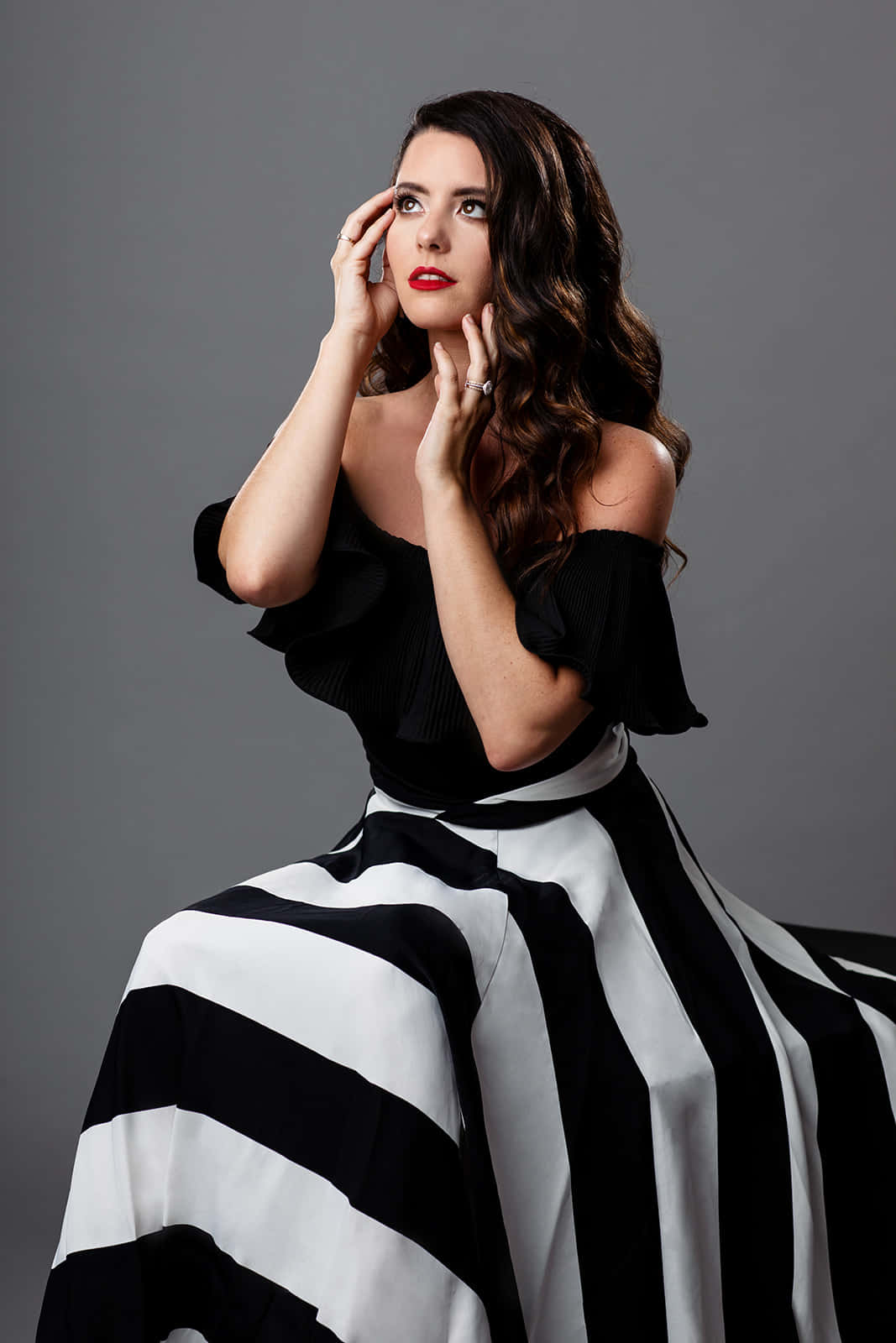 Black And White Fashion 桌布 壁紙 — 一位身穿黑色上衣和醒目黑白條紋裙的女性，在灰色中性攝影棚背景下優雅地擺姿勢。