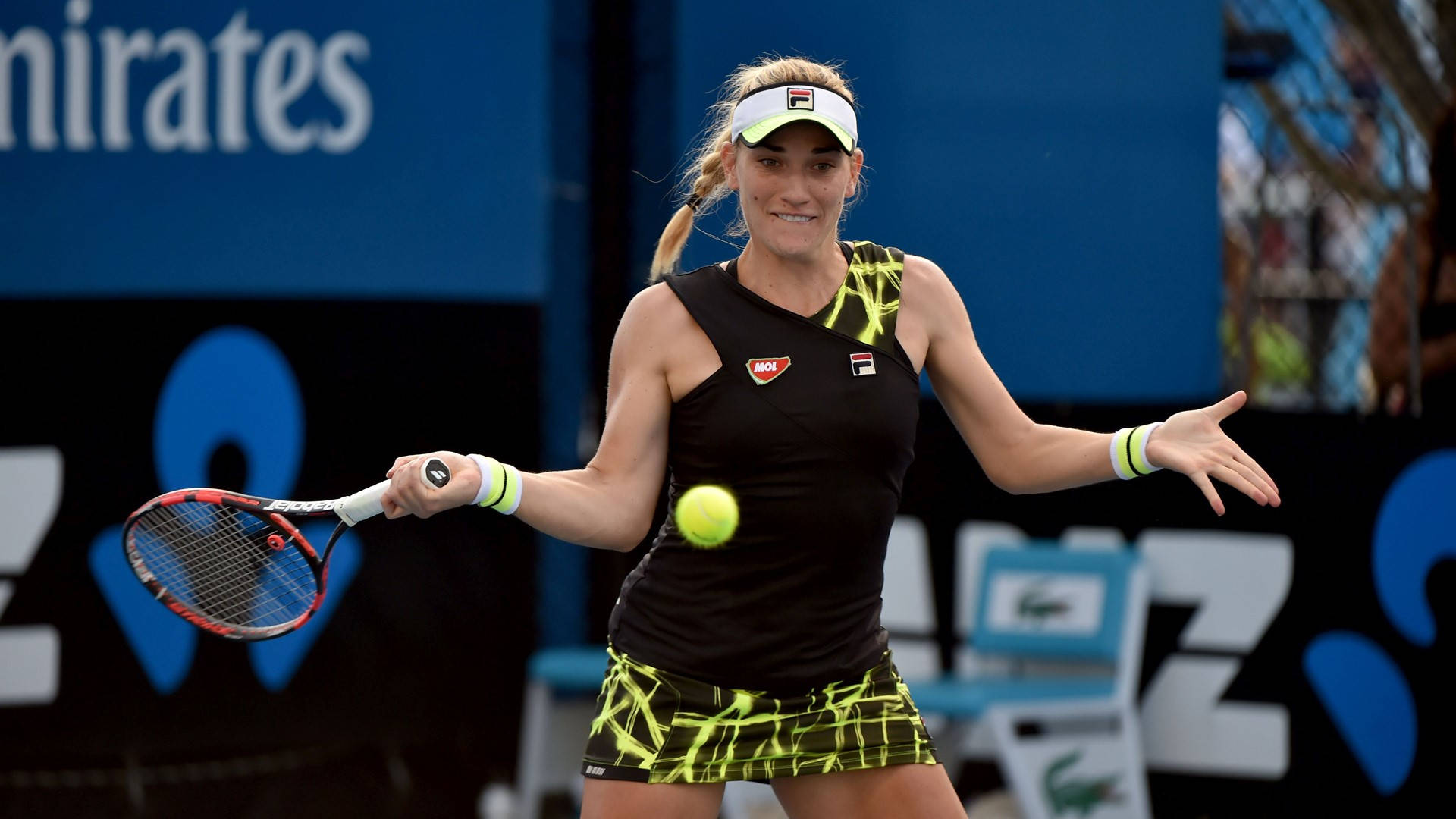 Australian Open 桌布 壁紙 — 一位身穿黑色和螢光黃色裝備的女網球選手在藍色球場上揮拍擊打空中明亮的黃色網球。