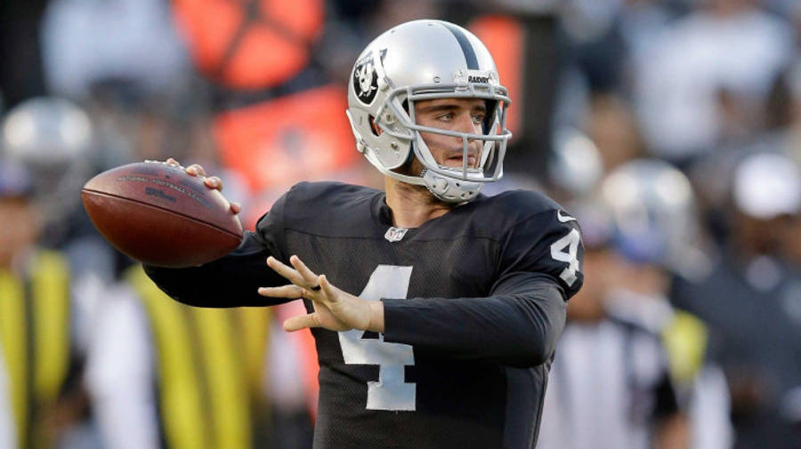 NFL 桌布 壁紙 — 一位身穿黑色和銀色制服的美式足球四分衛在比賽中準備投球，背景是模糊的體育場人群。