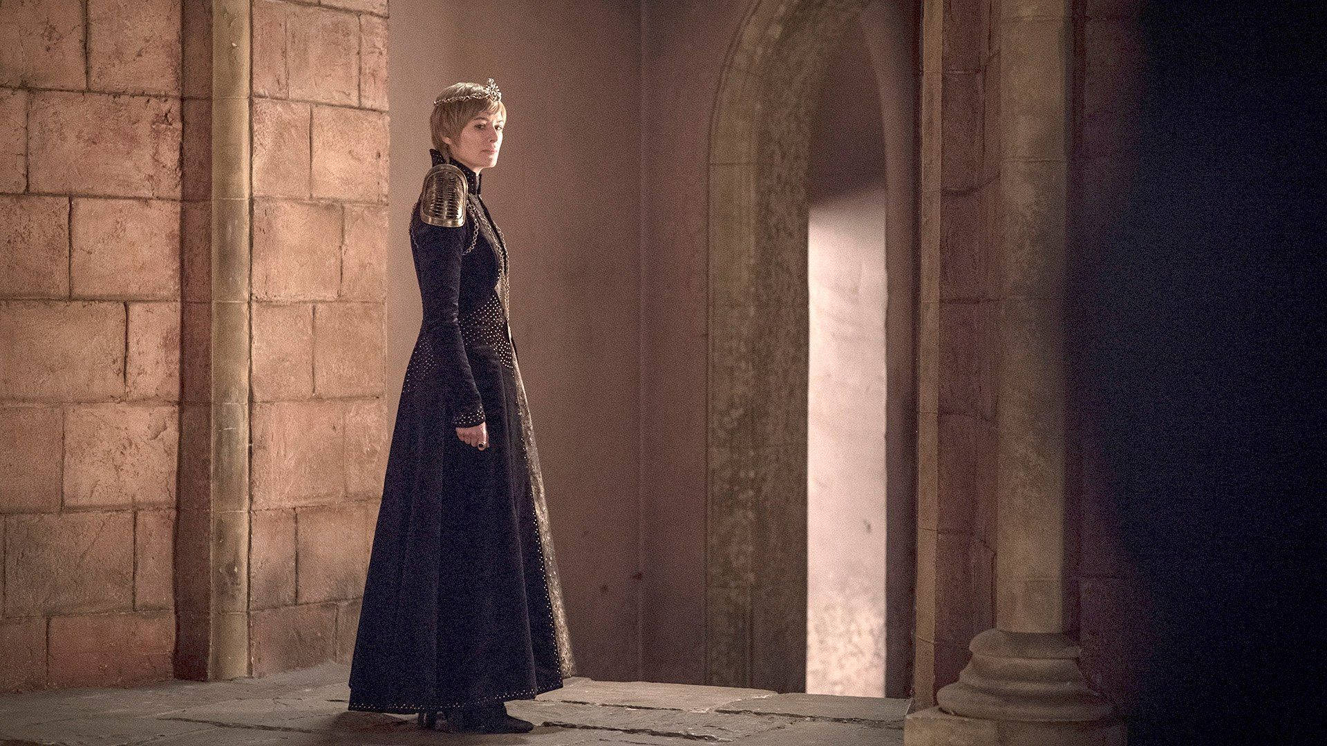 cersei lannister 桌布 壁紙 — 一位身穿黑色圖案長裙的女性站在石拱門中，沐浴在來自後方的溫暖光線中。