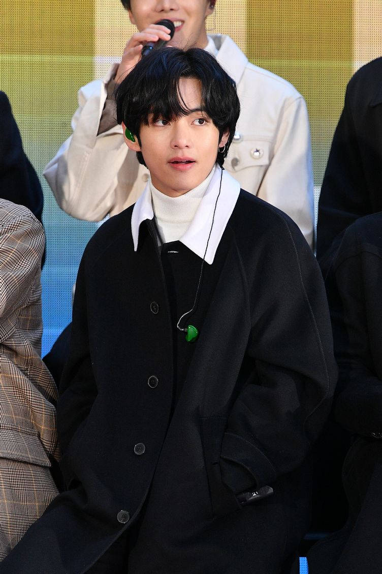 BTS 桌布 壁紙 — 一位身穿黑色外套和白色高領毛衣的年輕男子，在明亮的黃色背景活動中專注地坐著。