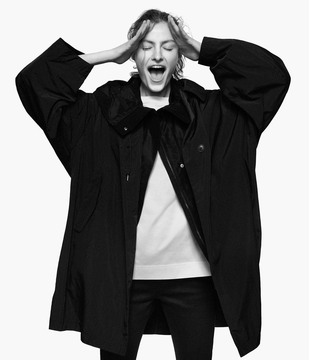 Uniqlo 桌布 壁紙 — 一位身穿黑色外套的女性，在純白背景前雙手放在頭上，張大嘴巴打哈欠。
