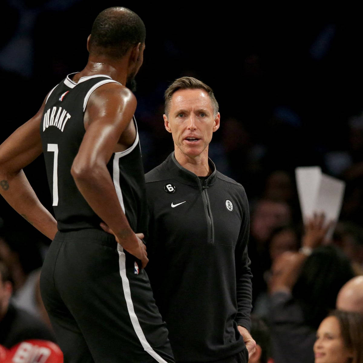 NBA 桌布 壁紙 — 一位身穿黑色外套的籃球教練在明亮的場館燈光下，在比賽中專注地與球員凱文·杜蘭特交談。