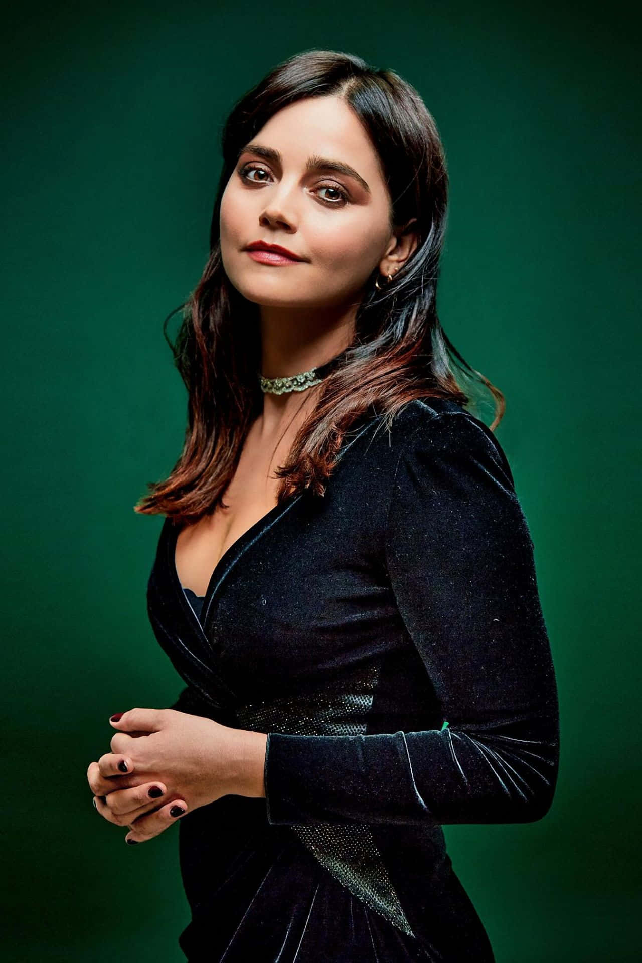 Jenna Coleman 桌布 壁紙 — 一位身穿黑色天鵝絨連衣裙的優雅女士，站在深綠色背景前，搭配柔和的工作室燈光。
