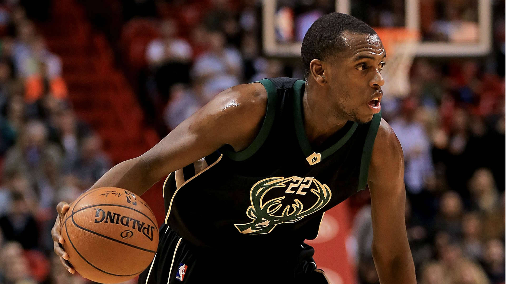 Khris Middleton 桌布 壁紙 — 一位身穿黑色密爾瓦基公鹿隊球衣的專注籃球運動員，在比賽中激烈運球，背景是模糊的人群。