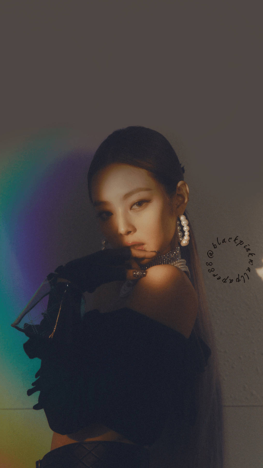 Jennie 桌布 壁紙 — 一位身穿黑色服裝、戴著珍珠耳環的女性，靠著背後有柔和彩虹光線的牆壁站立。