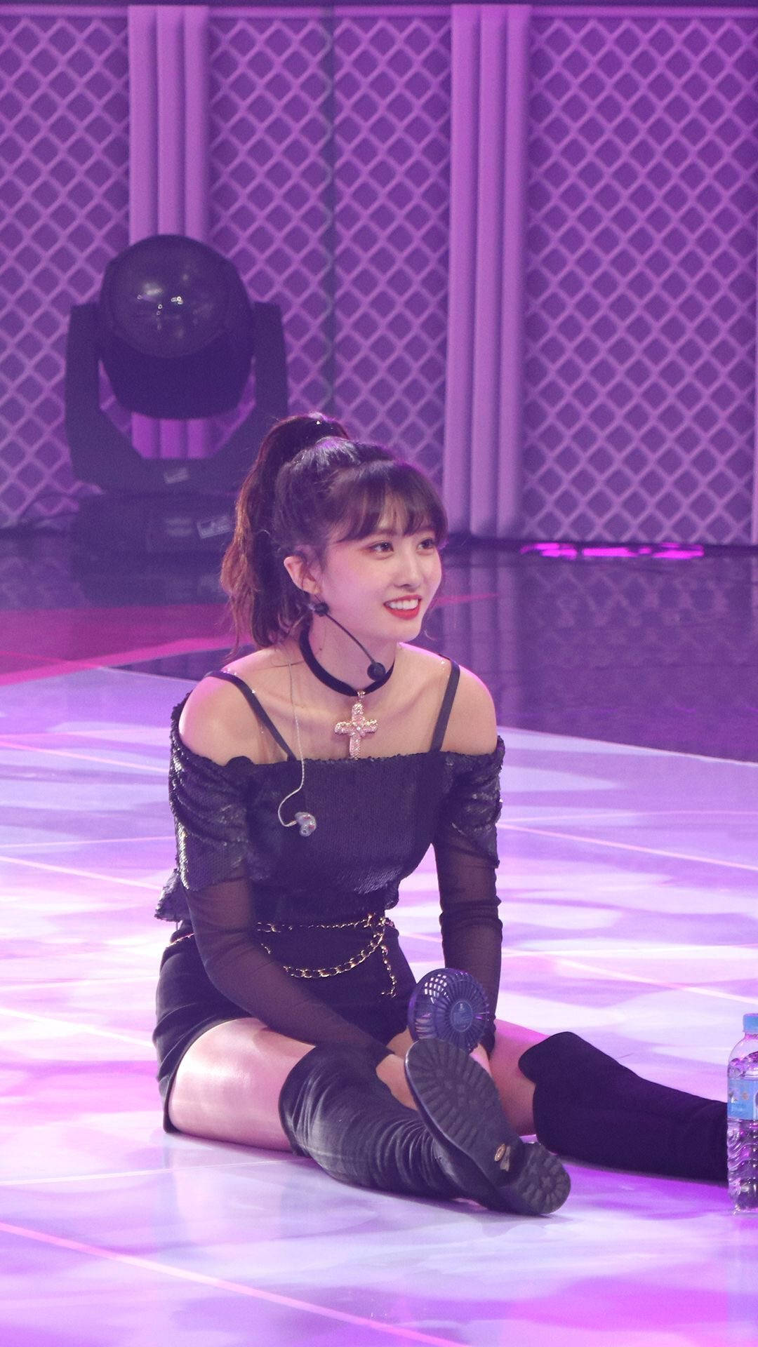 Momo 桌布 壁紙 — 一位身穿黑色服裝、面帶微笑的表演者坐在紫色燈光的舞台上，身後有一盞聚光燈。