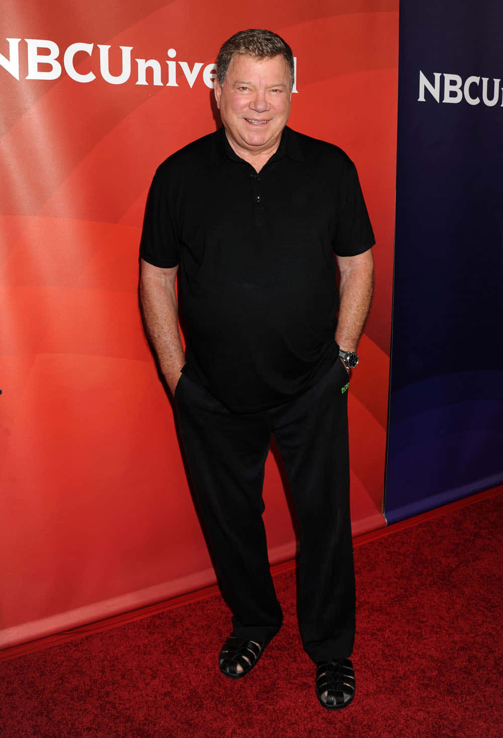 william shatner 桌布 壁紙 — 一位身穿黑色服裝的微笑男子自信地站在NBCUniversal品牌背景前的紅地毯上。