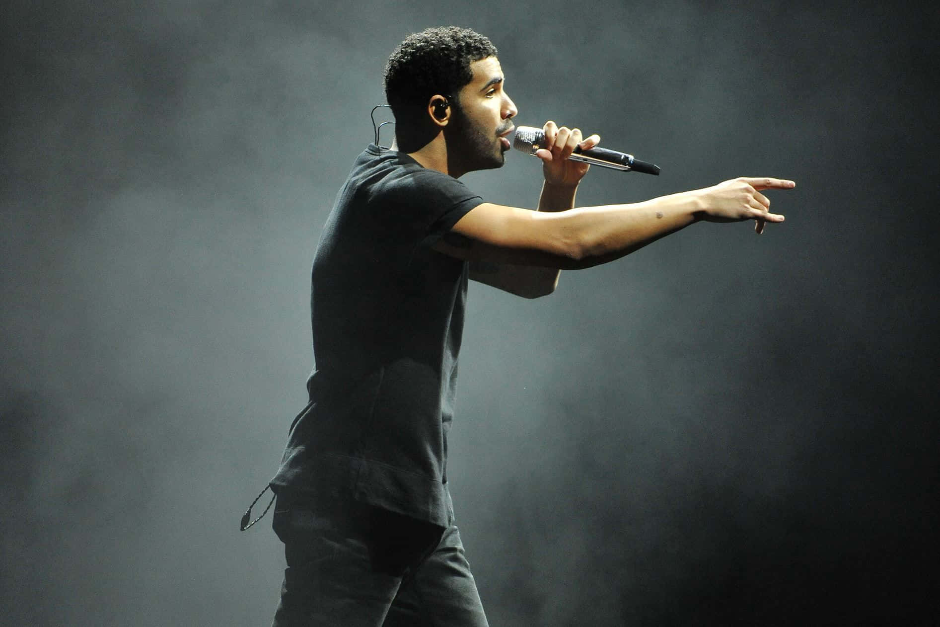 Drake 桌布 壁紙 — 一位身穿黑色服裝的男歌手在戲劇性的舞台燈光下，手持麥克風並向前指著表演。