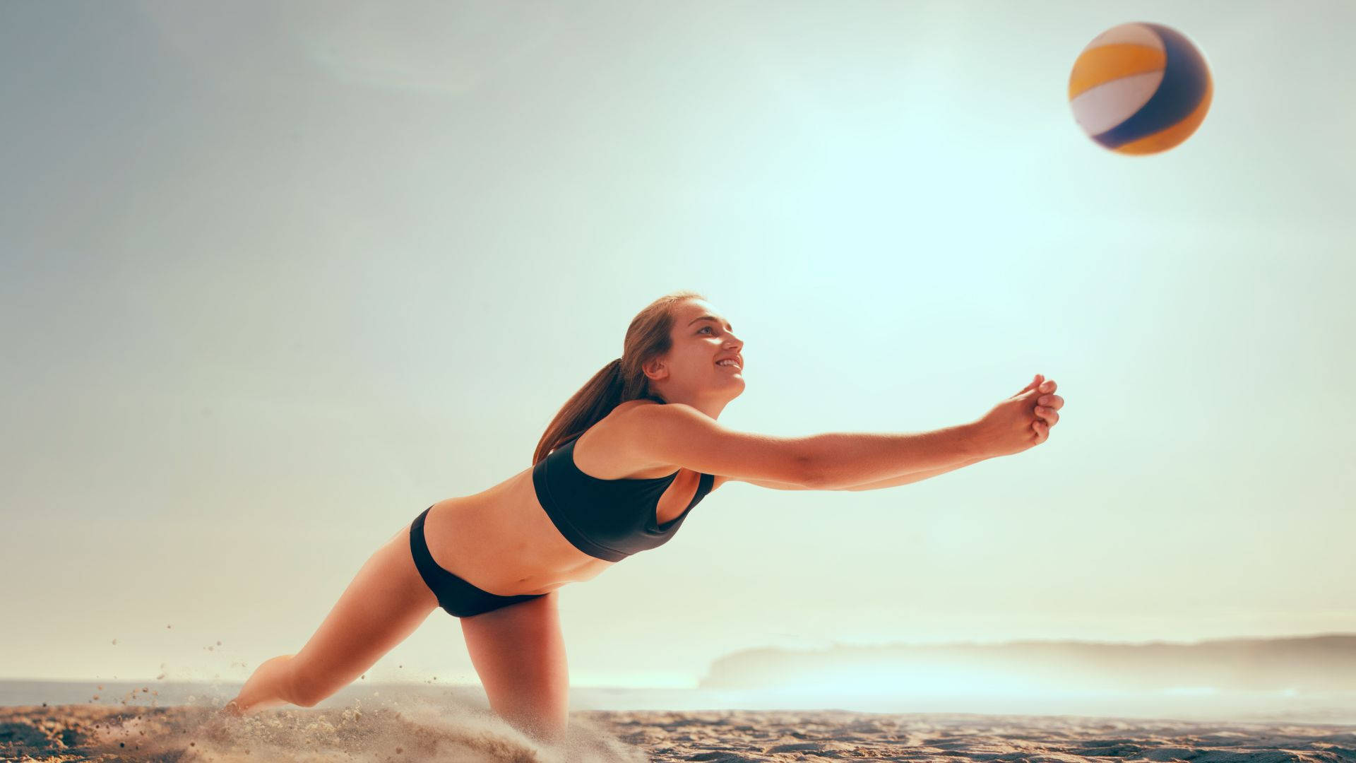 Volleyball Aesthetic 桌布 壁紙 — 一位身穿黑色比基尼的女性在陽光明媚的海灘上潛水，以專注的能量擊打排球。