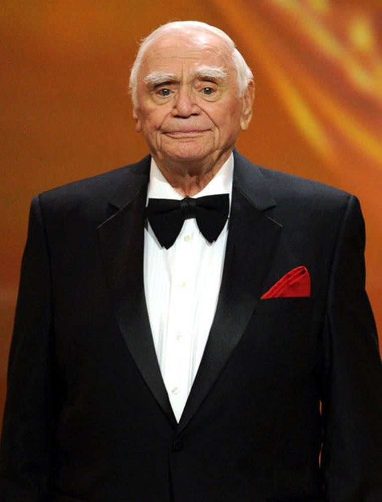 actor 桌布 壁紙 — 一位身穿黑色燕尾服、佩戴紅色口袋方巾的年長男性，站在溫暖的橙色背景前。