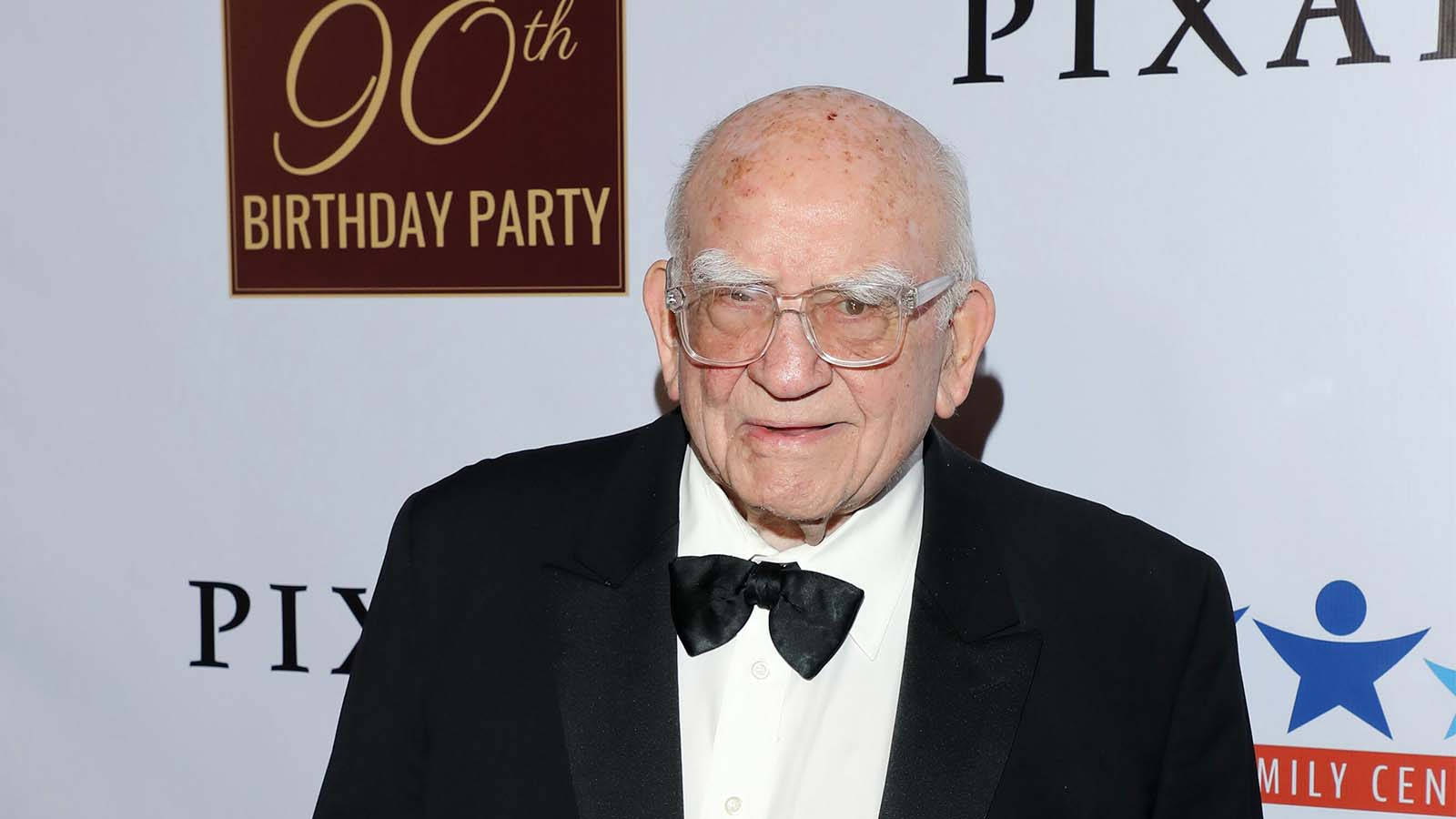 Tuxedo 桌布 壁紙 — 一位身穿黑色燕尾服和領結的長者，在Pixar 90歲生日派對背景前微笑。